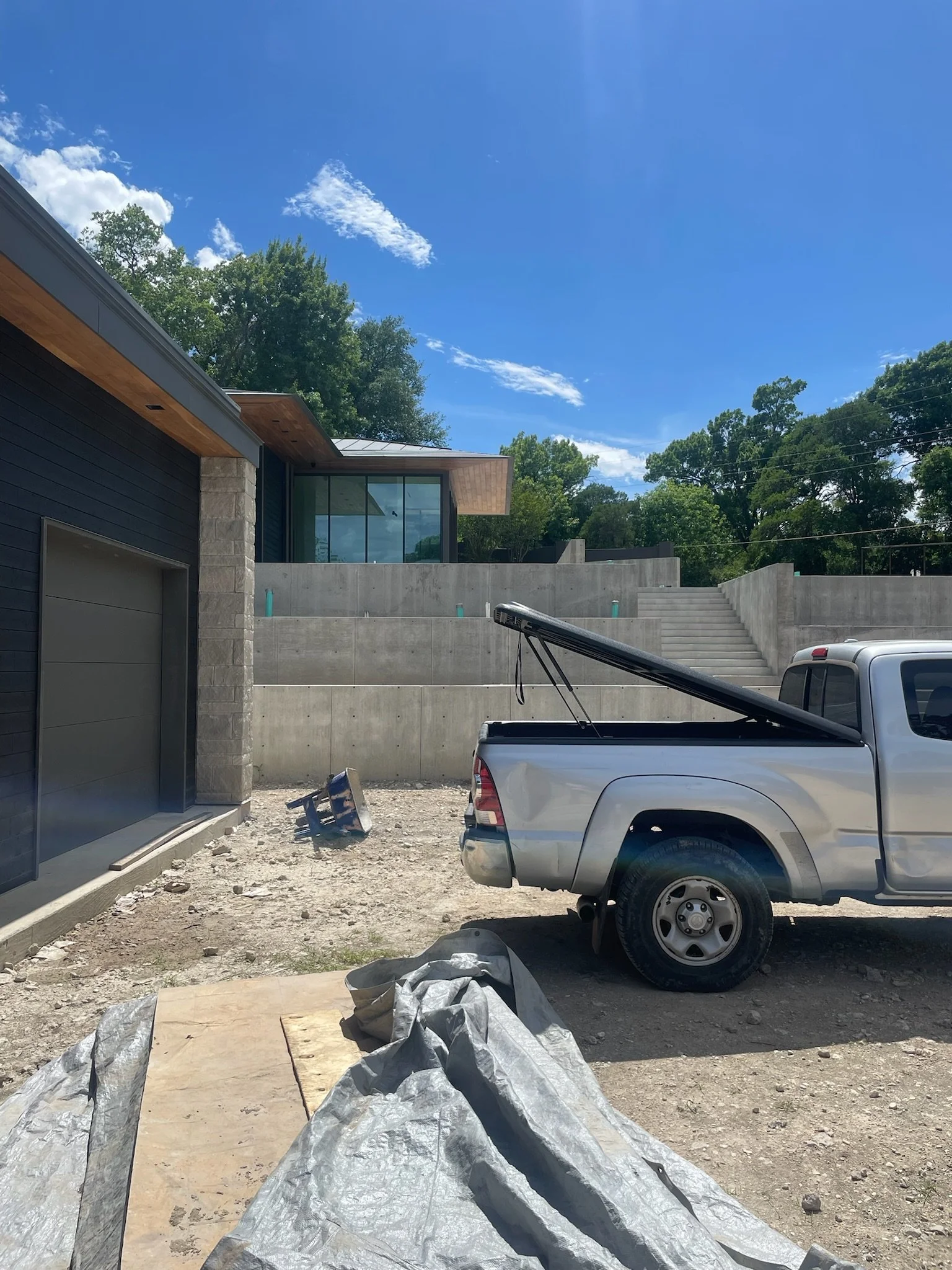 Construction site with a modern house, concrete stairs, a pickup truck, and construction materials on the ground under a blue sky with some clouds.