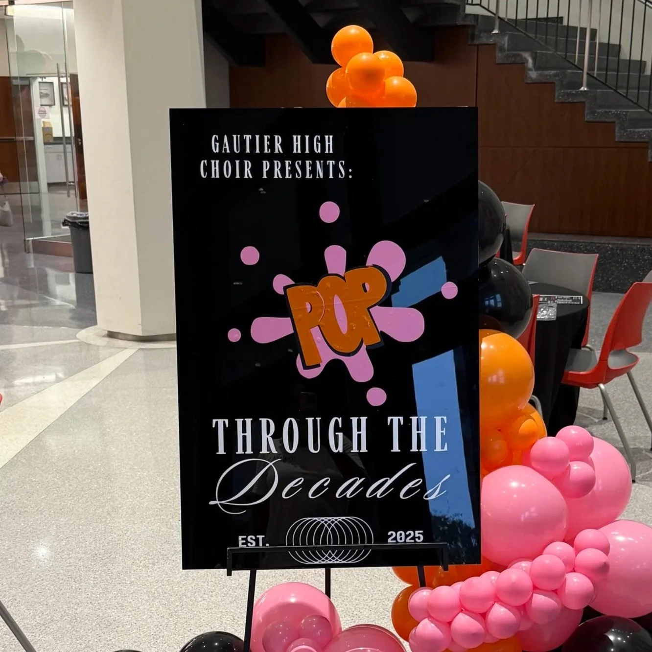 Sign for Gautier High Choir's pop concert, titled 'Pop Through the Decades,' with black background, colorful graphic elements, and pink, orange, and black balloons.