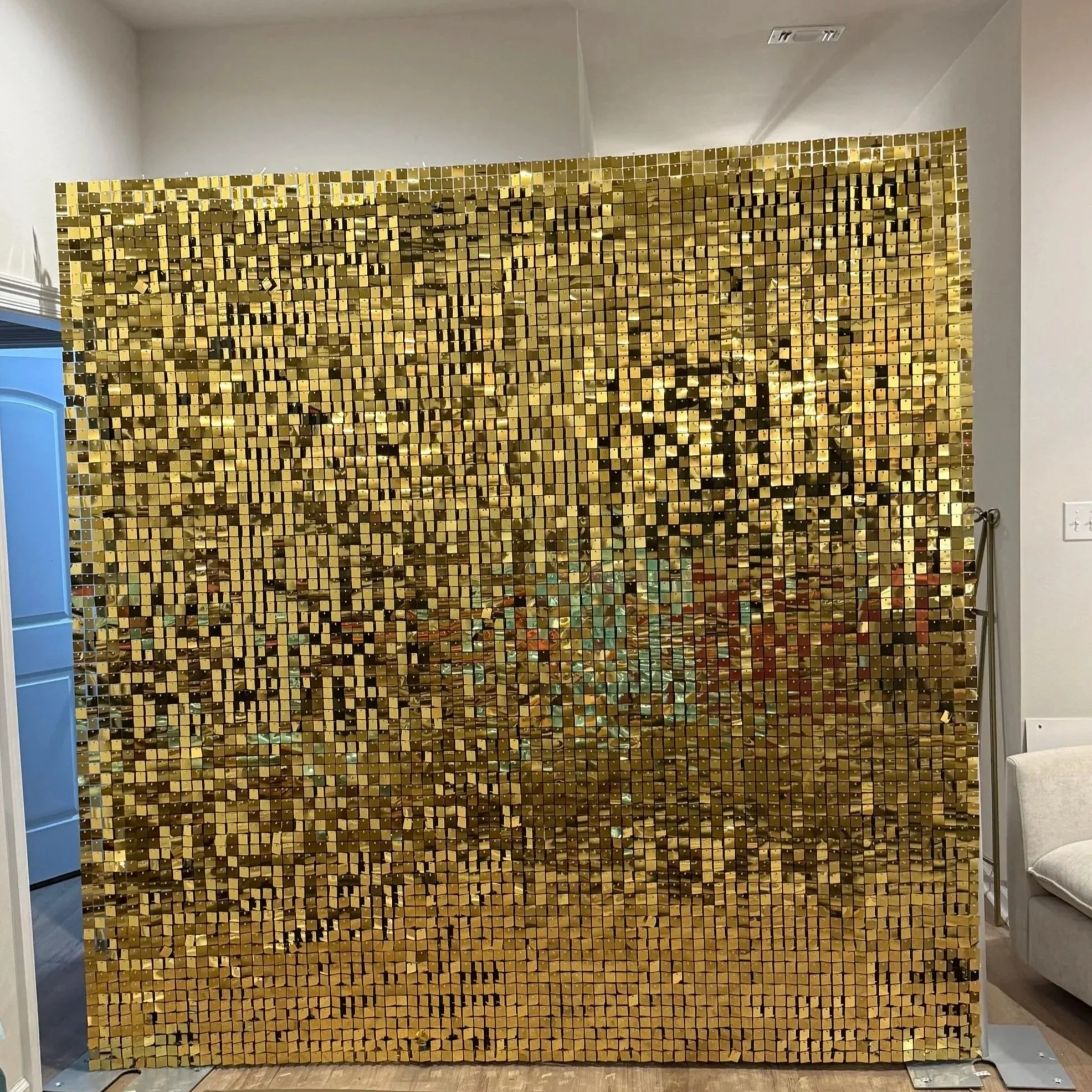 A decorative wall installation made of small, shiny gold square tiles arranged in a grid, covering a large section of a room's wall.