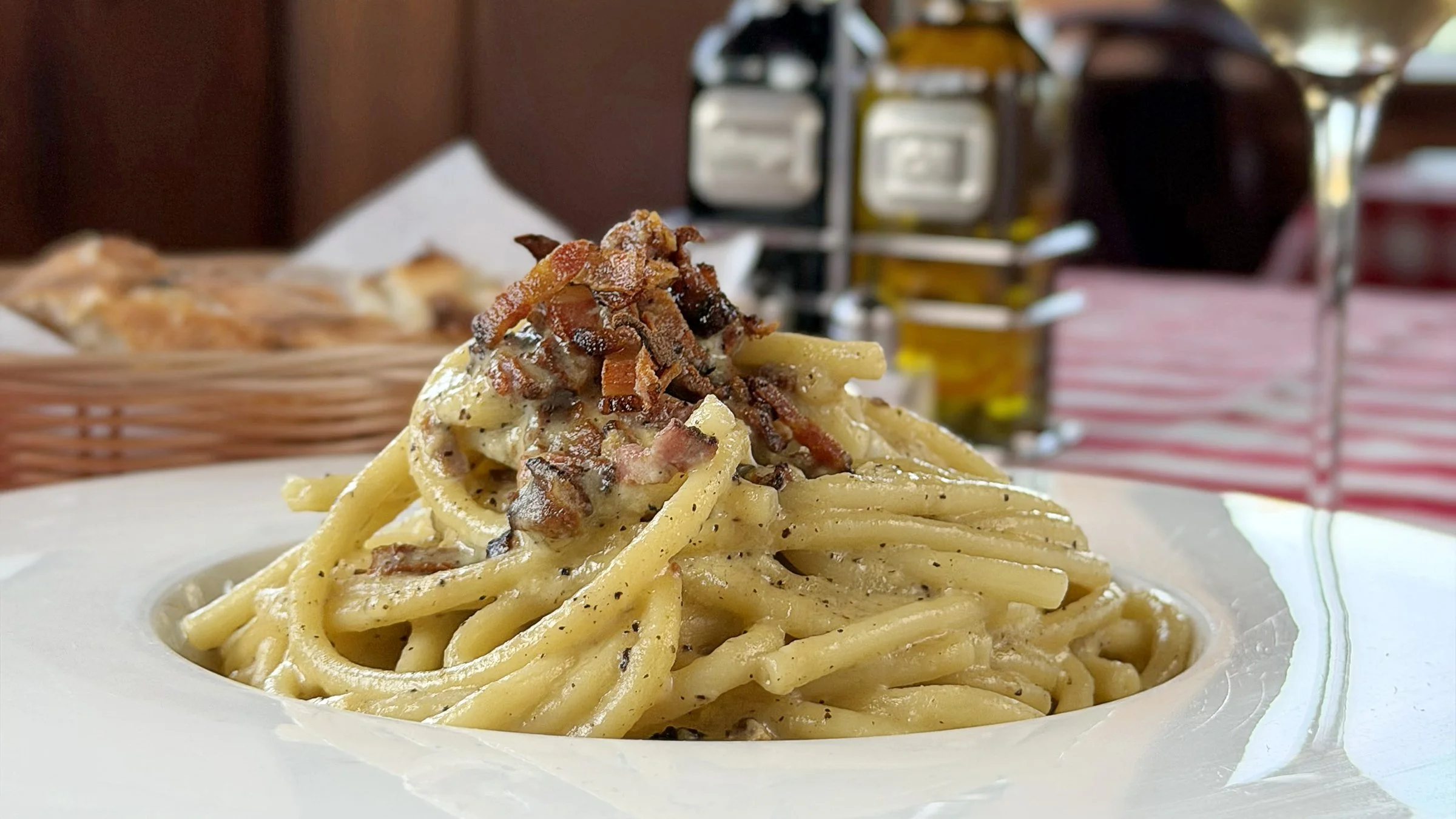 Close-up of a plate of creamy pasta topped with bacon bits, in a restaurant setting.