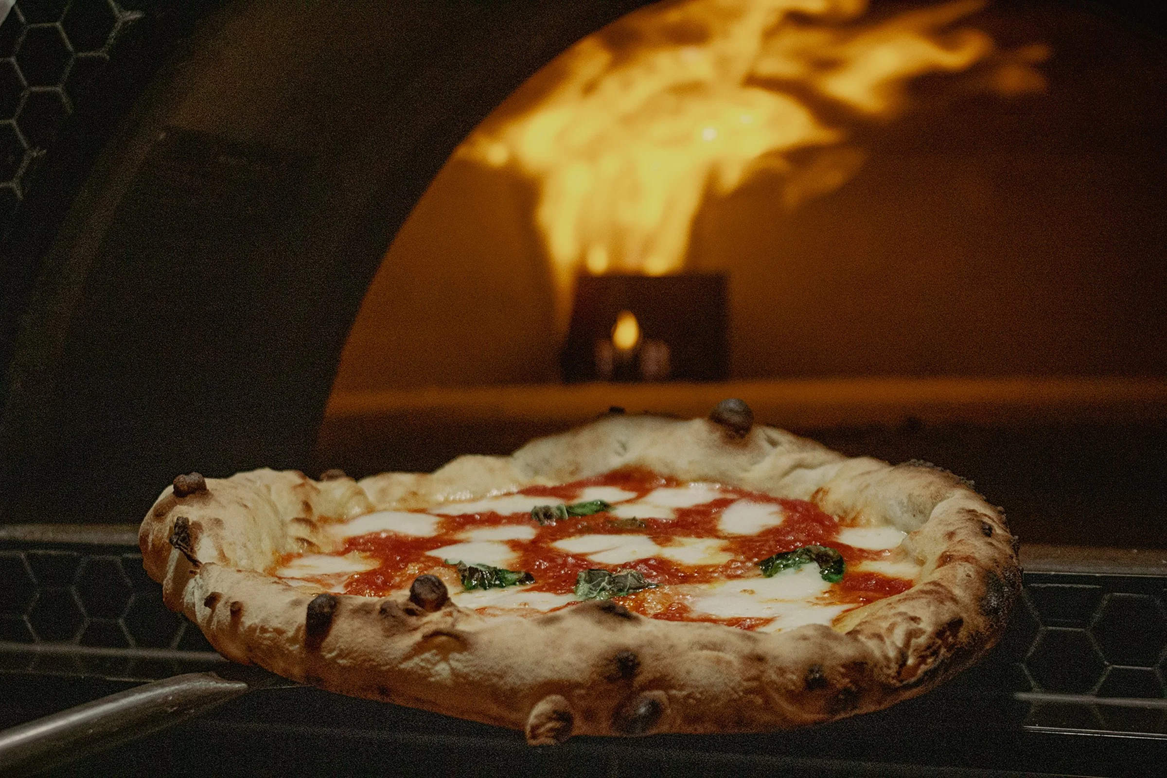 Pizza baking inside an oven with flames visible in the background.