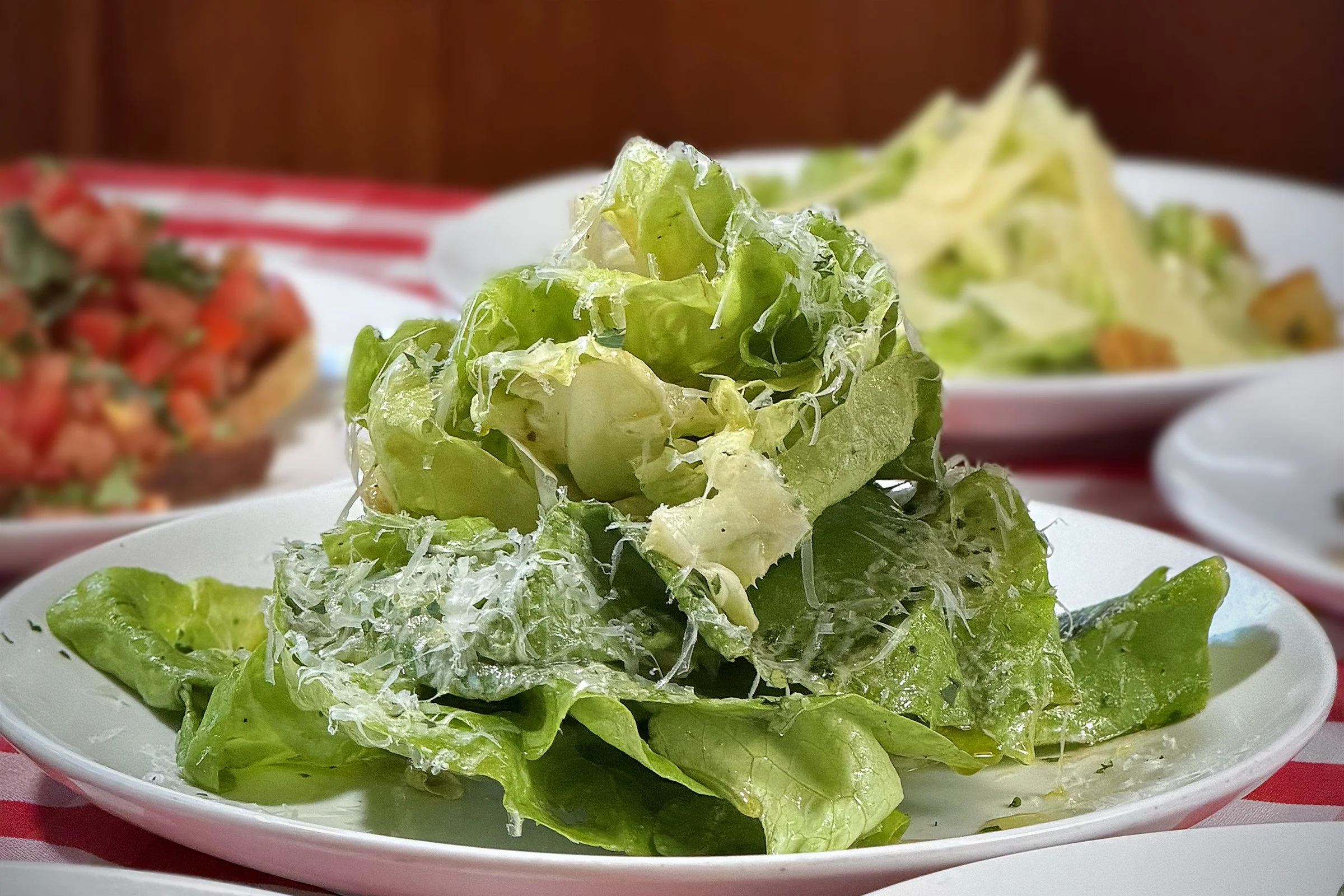 Fresh green lettuce salad with shredded cheese served on a white plate with other dishes in the background.