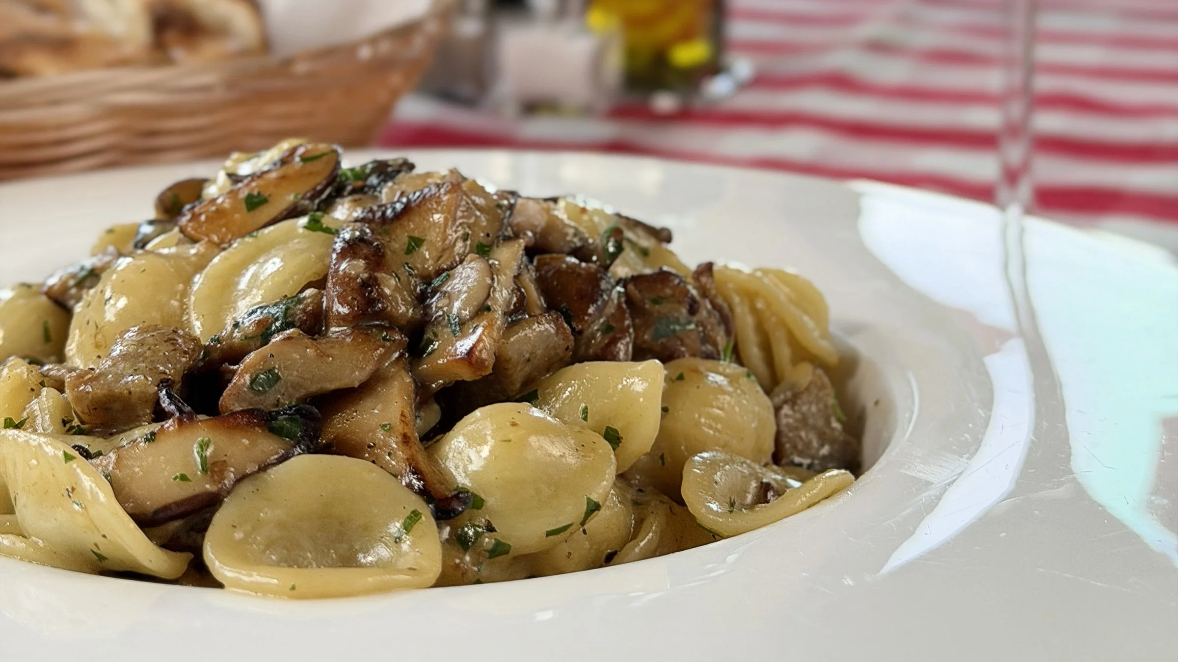 Plate of cooked orecchiette pasta with sautéed mushrooms and herbs.