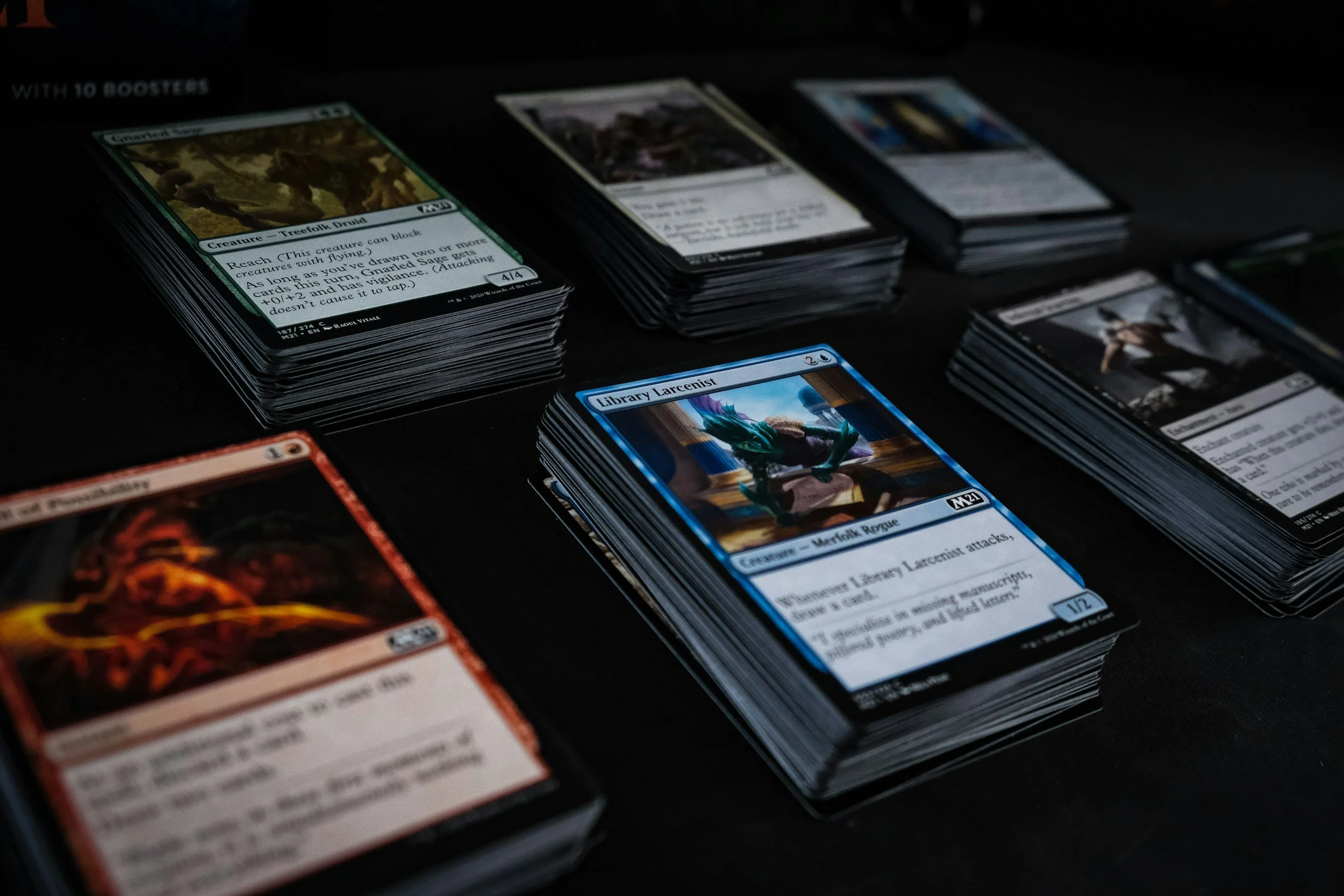 Stacks of Magic: The Gathering trading cards on a black surface, with some cards spread out and others in piles, featuring various artwork and card details.