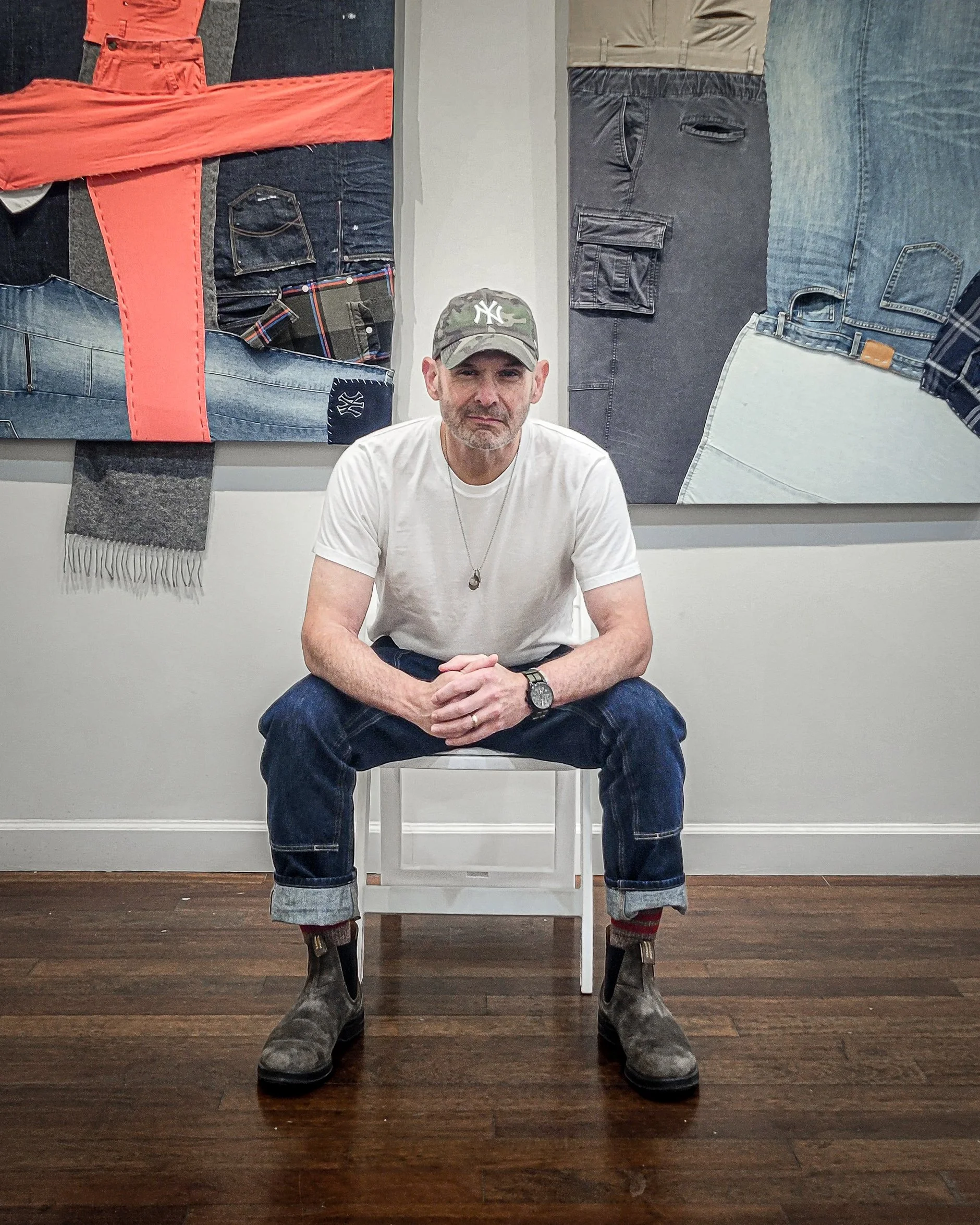Daniel Flahiff seated in art studio facing camera, white t-shirt, jeans, ball cap