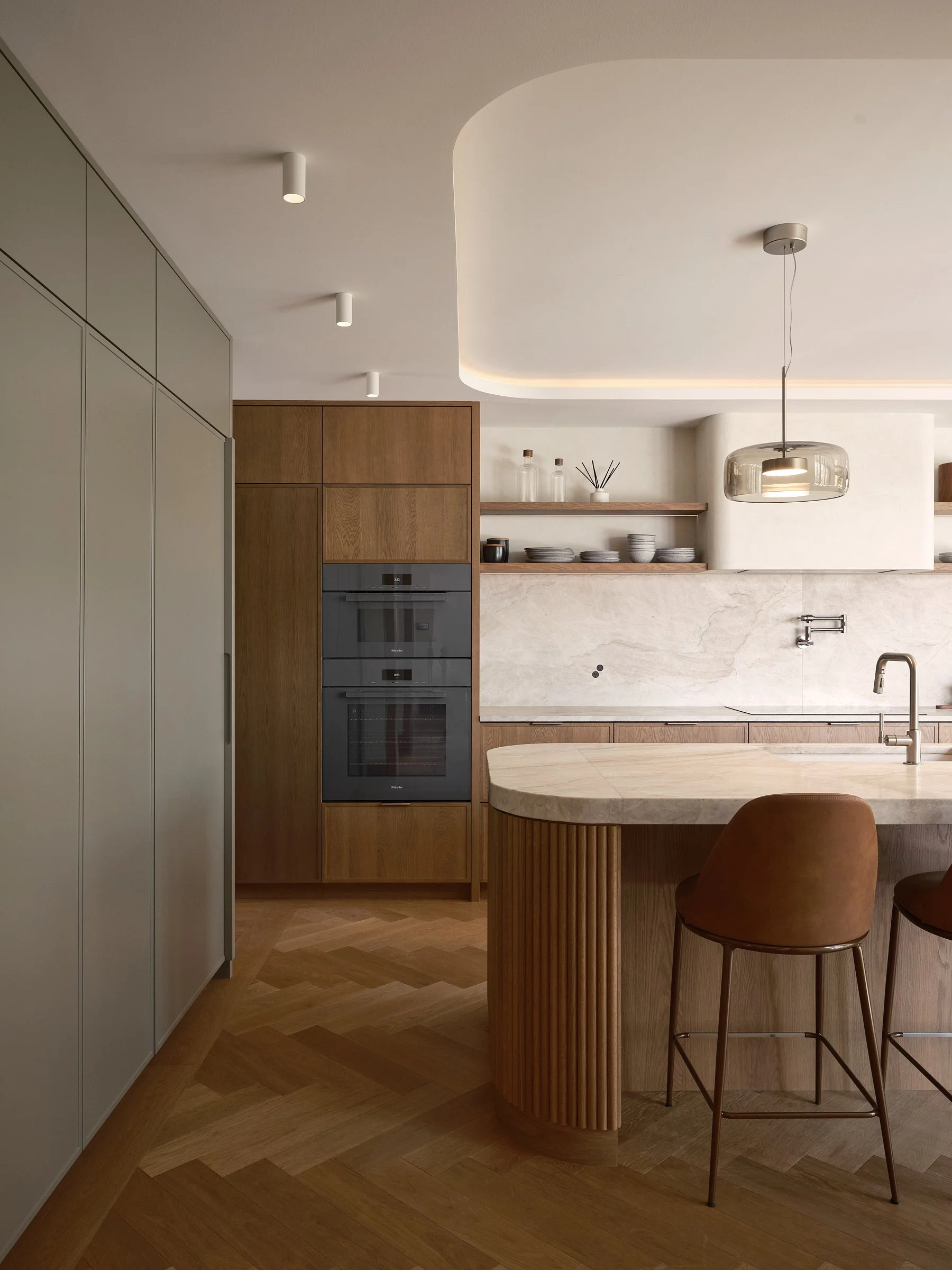 Cuisine sur mesure à Westmount avec îlot arrondi en pierre, façades en bois et mobilier intégré aux tons doux.