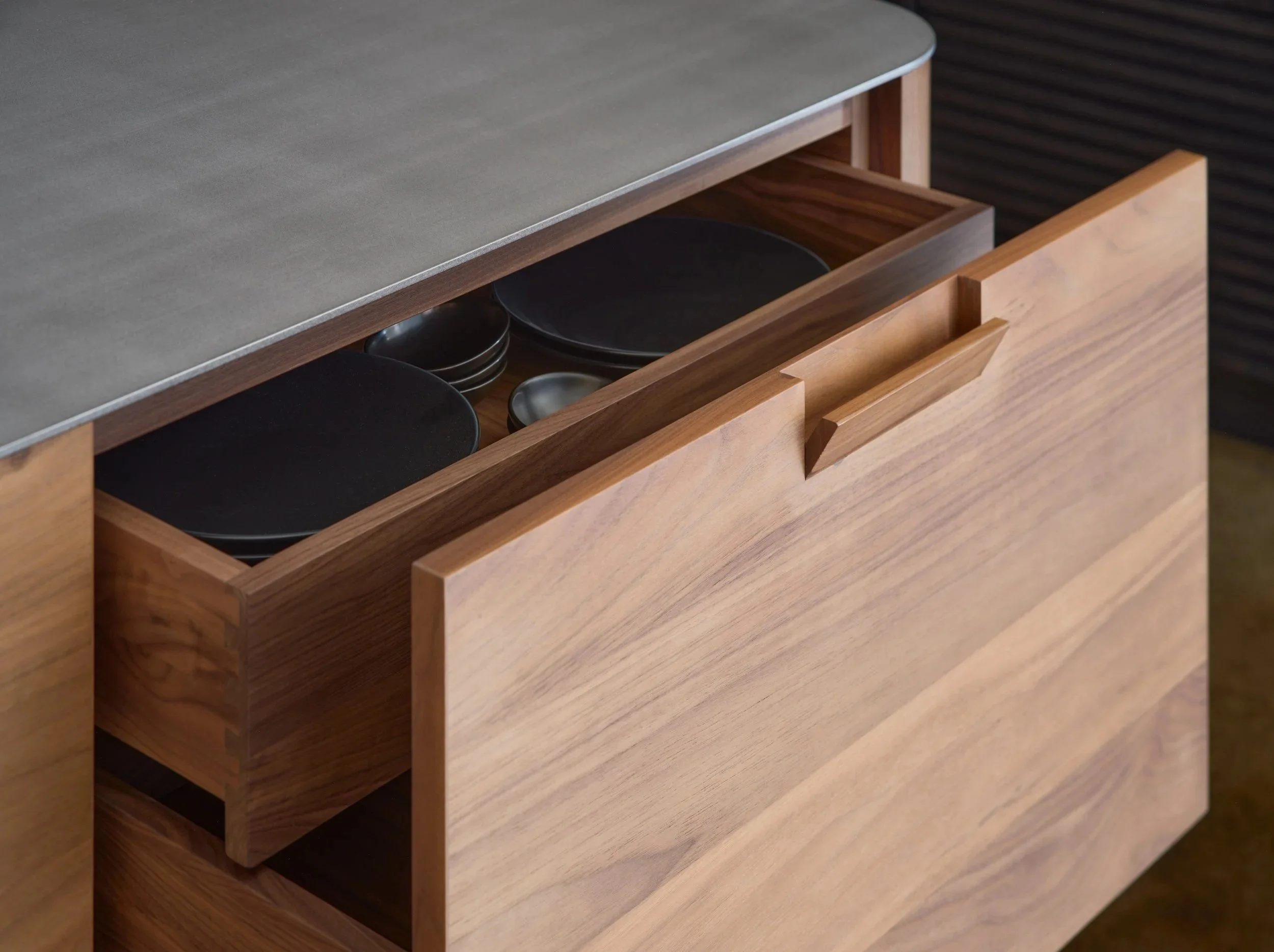Un meuble en bois avec un tiroir ouvert contenant des assiettes en céramique noire et grise.