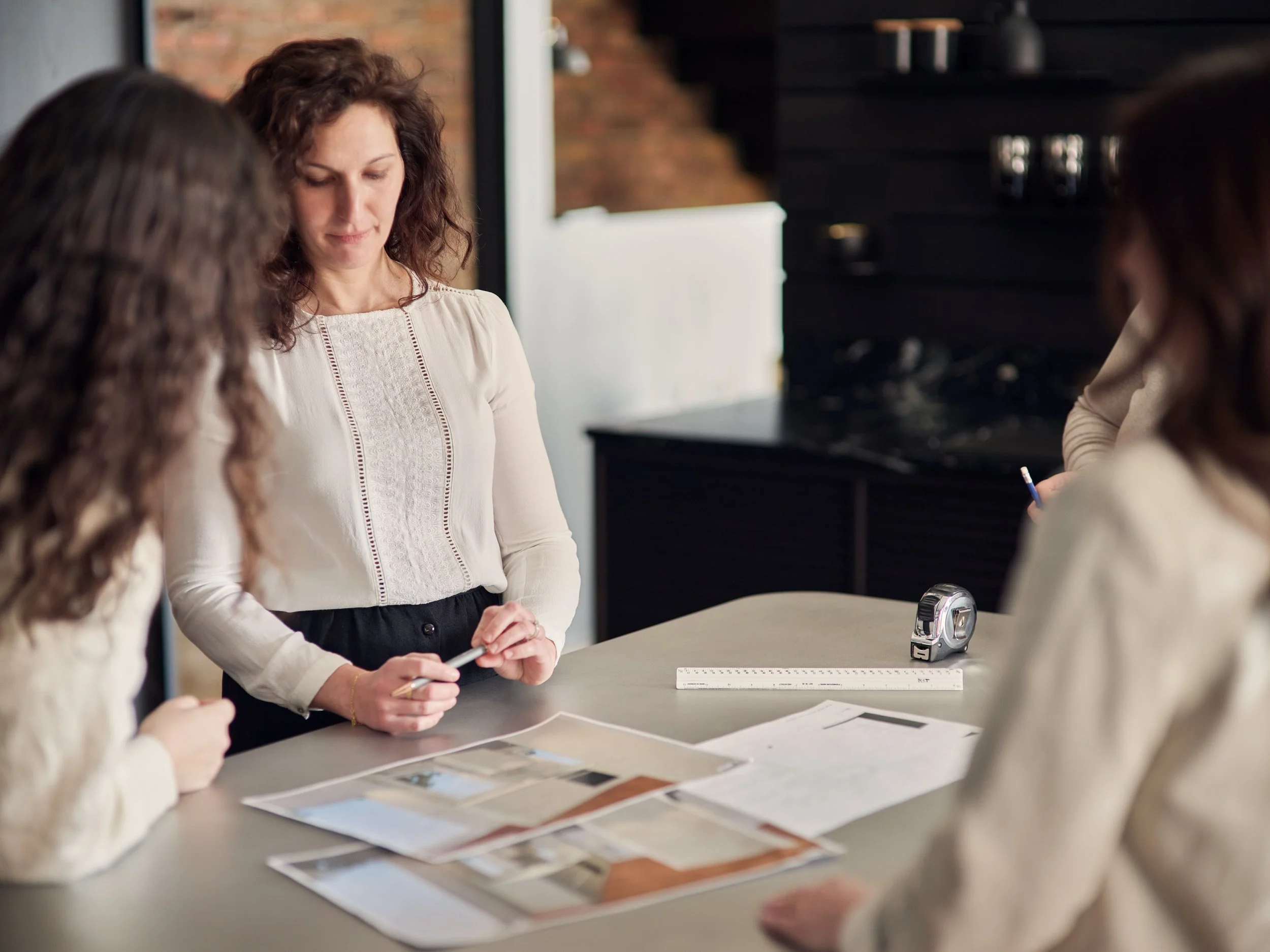 Designer cuisiniste échangeant avec des clientes autour des plans et des matériaux d’un projet de cuisine sur mesure.