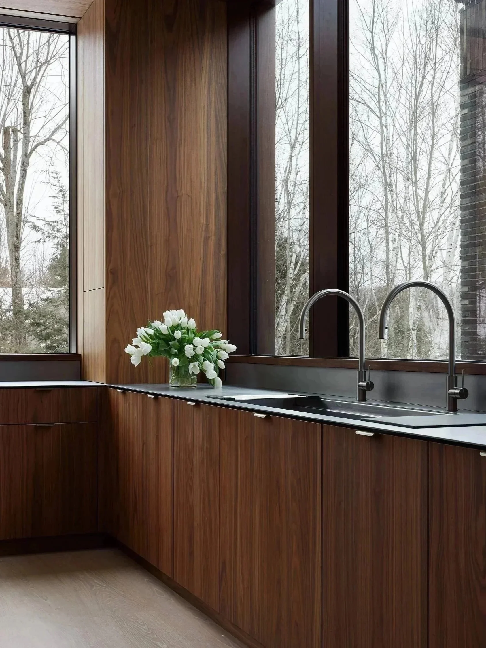 Cuisine sur mesure en noyer avec veinage naturel du bois et grandes fenêtres offrant une lumière abondante.