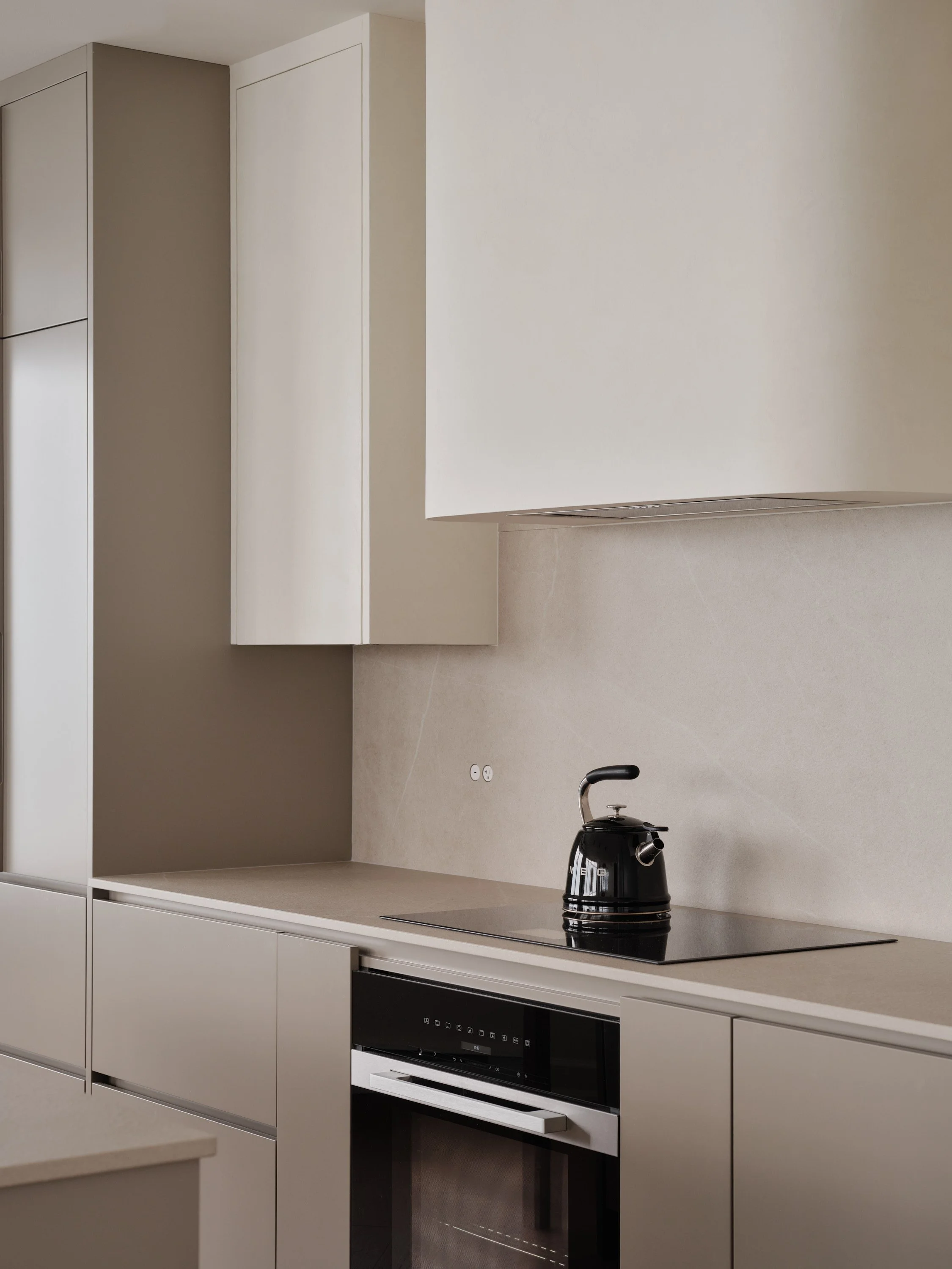 Cuisine contemporaine sur mesure avec armoires aux tons neutres et hotte aux angles arrondis.