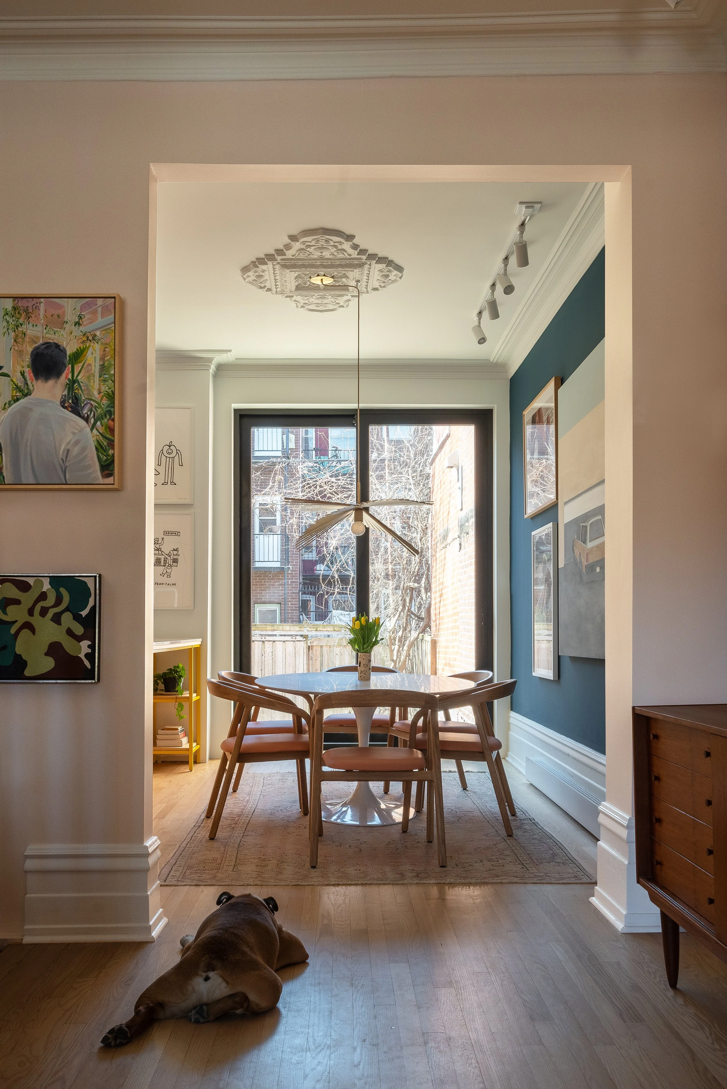 Dining room in an old house. Oval table, classic chairs, dark wall with gallery of paintings in a maximalist décor.