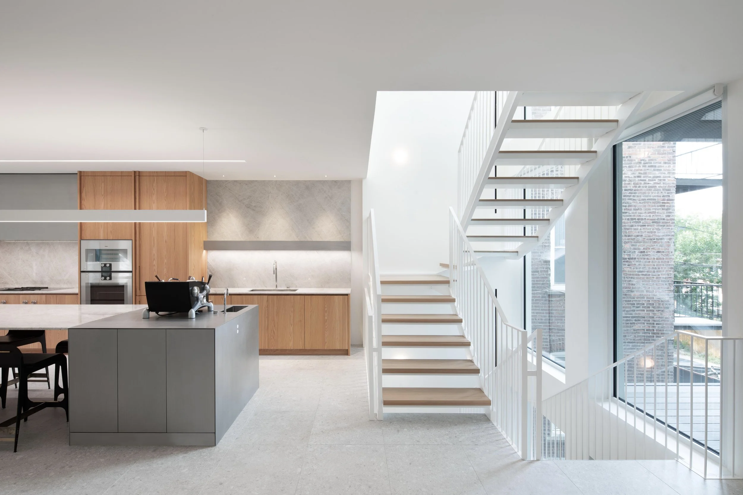 Intérieur moderne d'une cuisine ouverte avec escaliers blancs en bois, grands fenêtres et décor minimaliste.