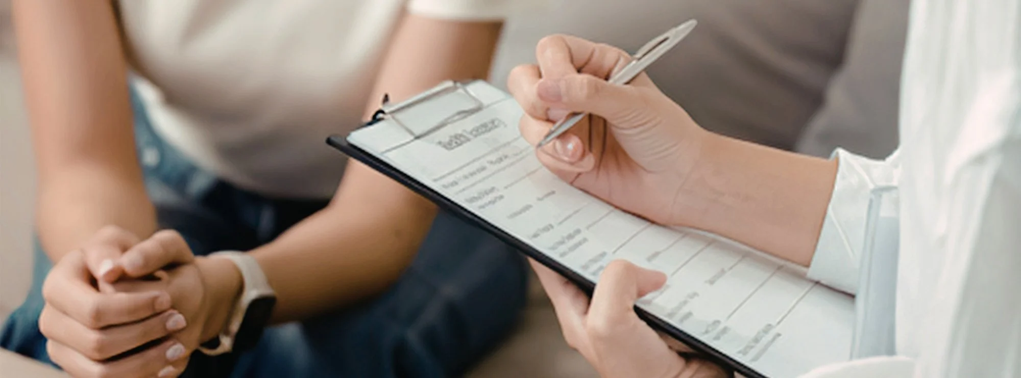 Close-up of a therapist holding a clipboard and pen during an intake session with a client, representing the seamless process of booking a marriage counseling near me free consultation.