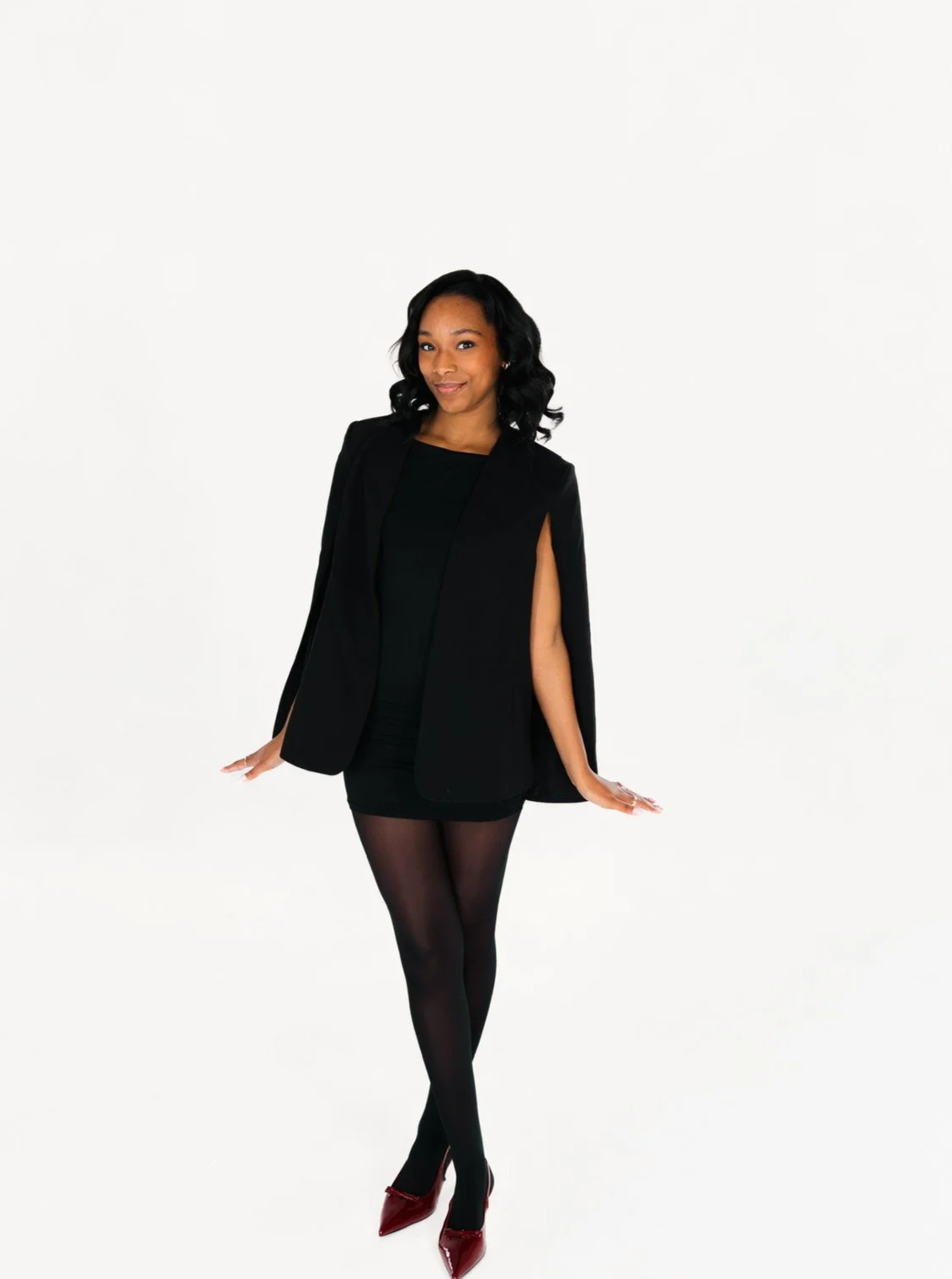 Young woman with long dark hair outdoors in spring, wearing a white strapless top and a necklace with a 'B' pendant.