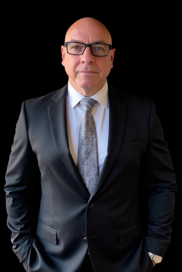 Bald man in a suit smiling against a neutral background.
