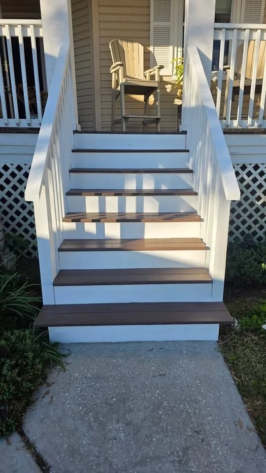 Front view of outdoor staircase leading to house porch with a wooden chair on the porch.