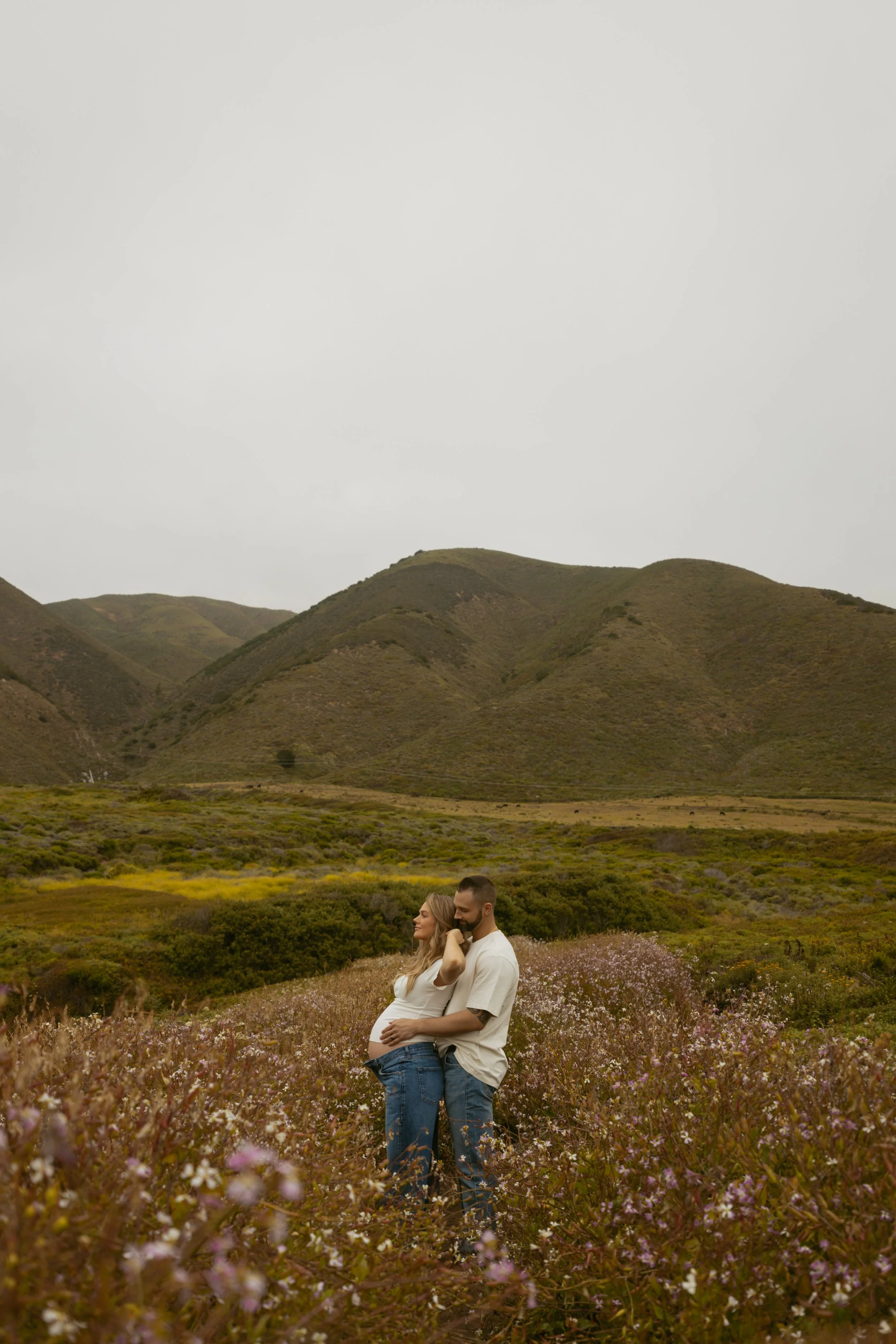 man and woman standing in wildflowers in big sur for babymoon photos during sunset photoshoot