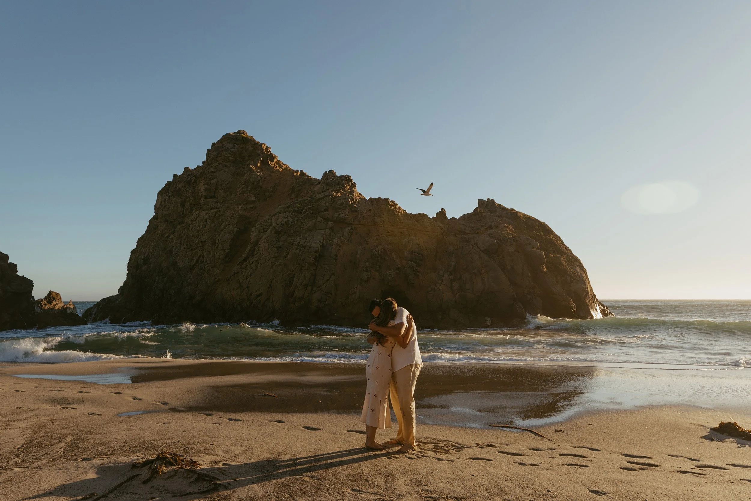 woman and man embracing in front of the Keyhole Arch after getting engaged on Pfeiffer Beach in Big Sur California