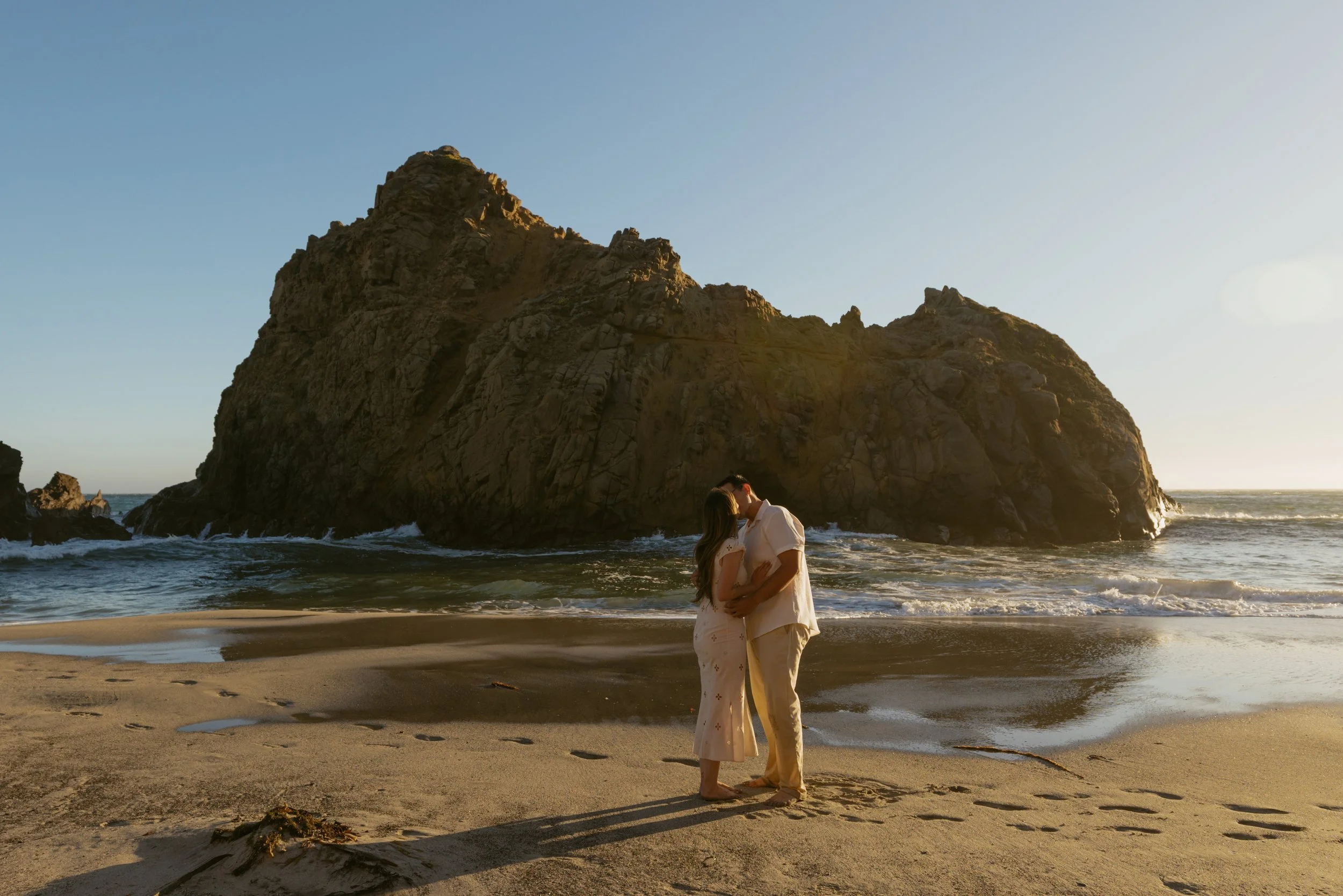 woman and man embracing in front of the Keyhole Arch after getting engaged on Pfeiffer Beach in Big Sur California