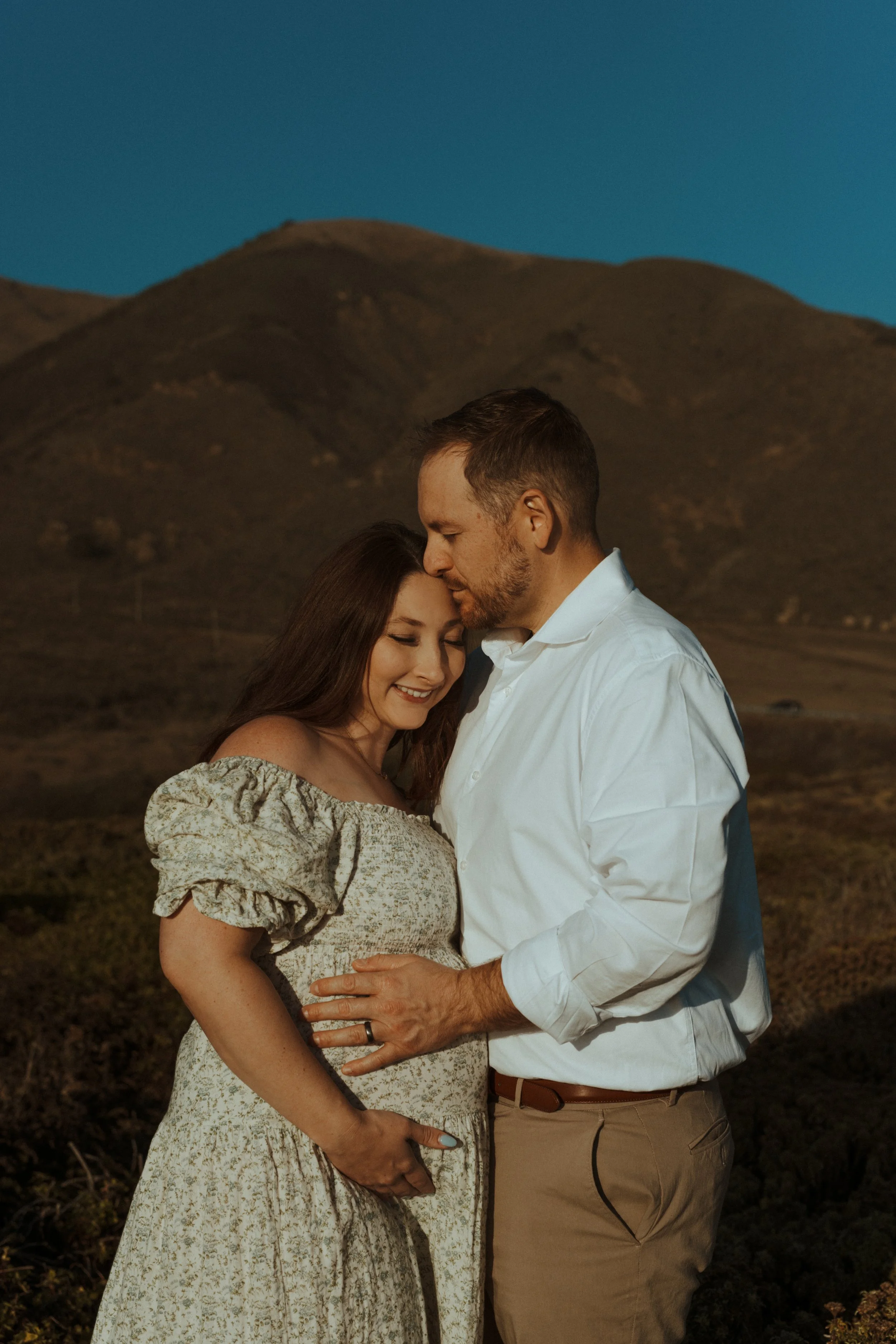 man holding wife's pregnant belly in big sur
