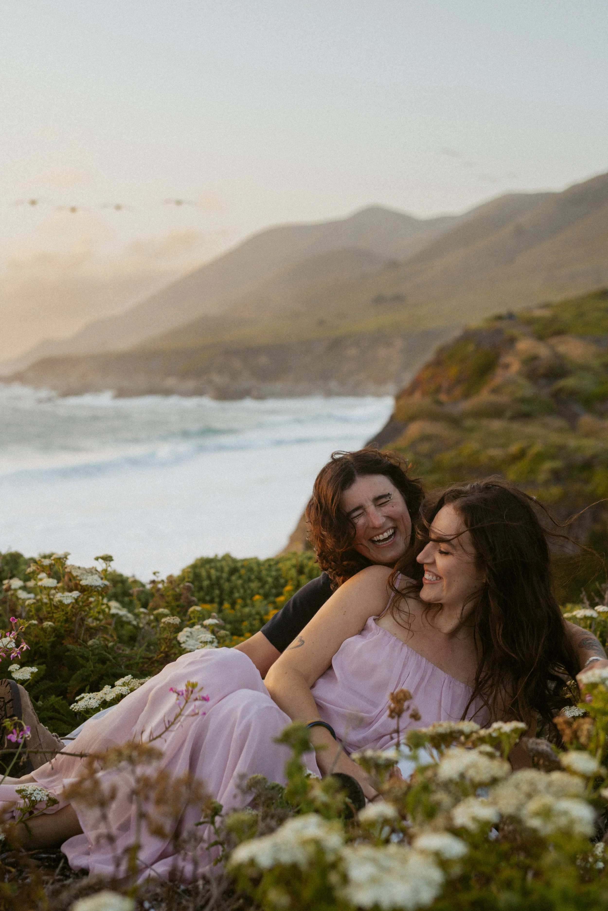 a lgbtq couple laying in wildflowers in big sur california during their engagement photoshoot