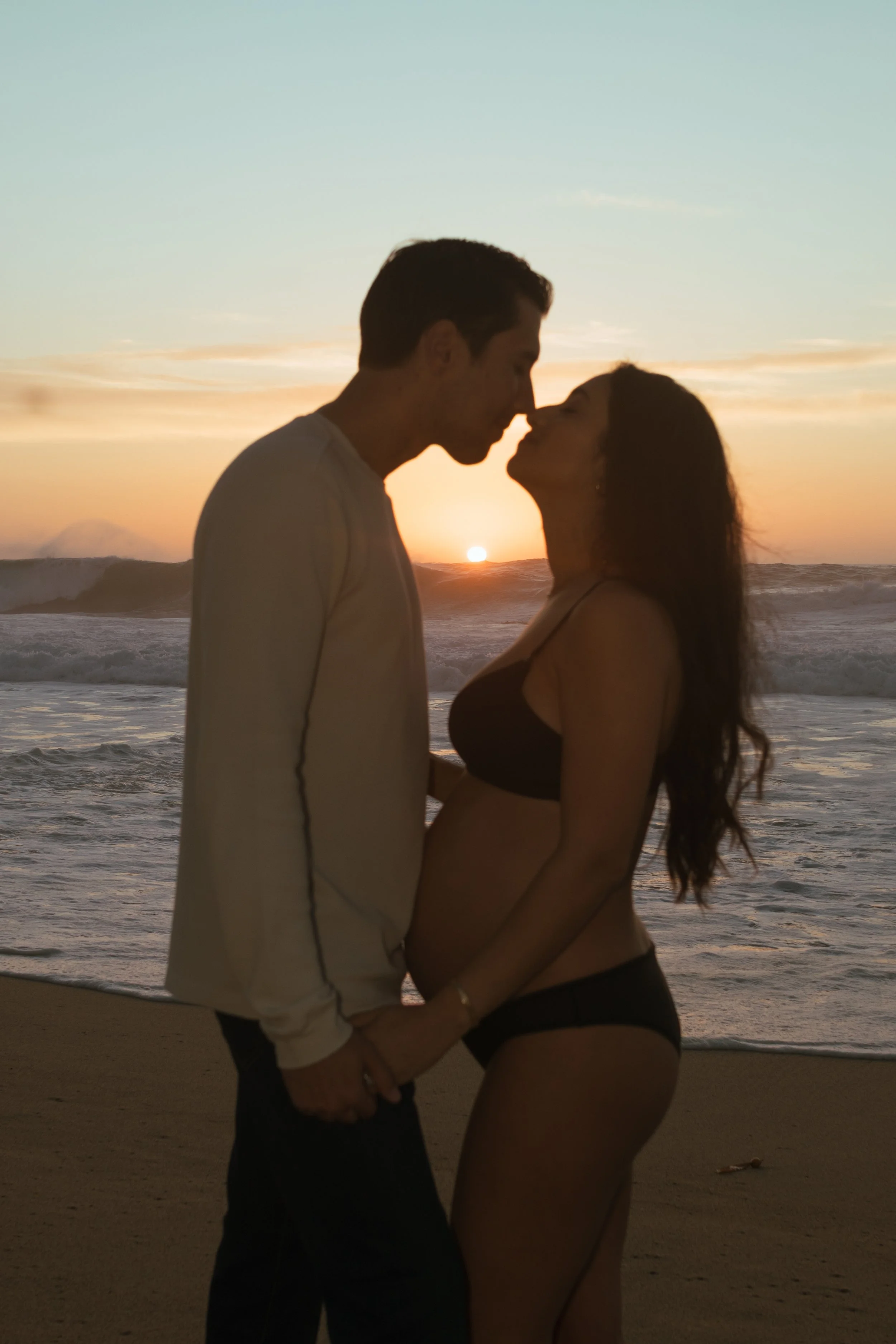 couple about to kiss in front of ocean in carmel california for maternity photoshoot
