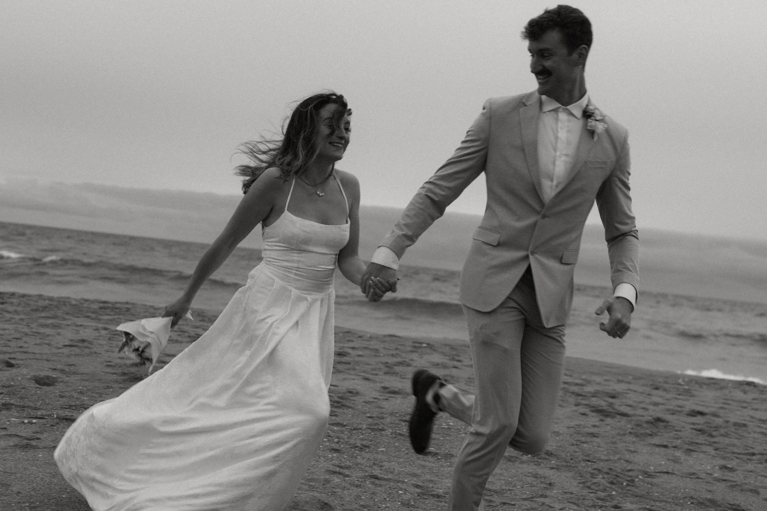 bride and groom running down beach after big sur small wedding