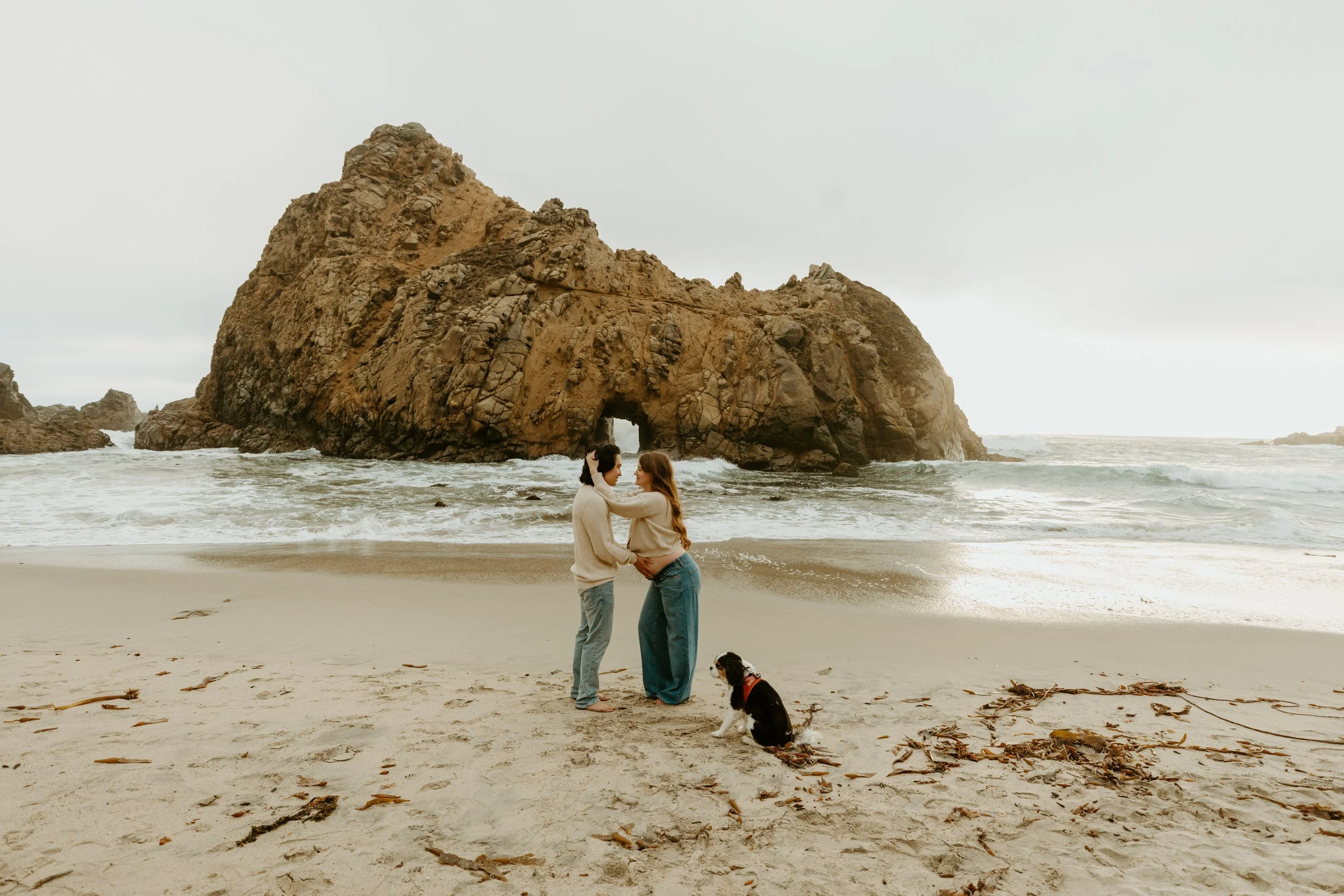 couple embracing in front of pfeiffer keyhole arch in big sur for maternity photoshoot