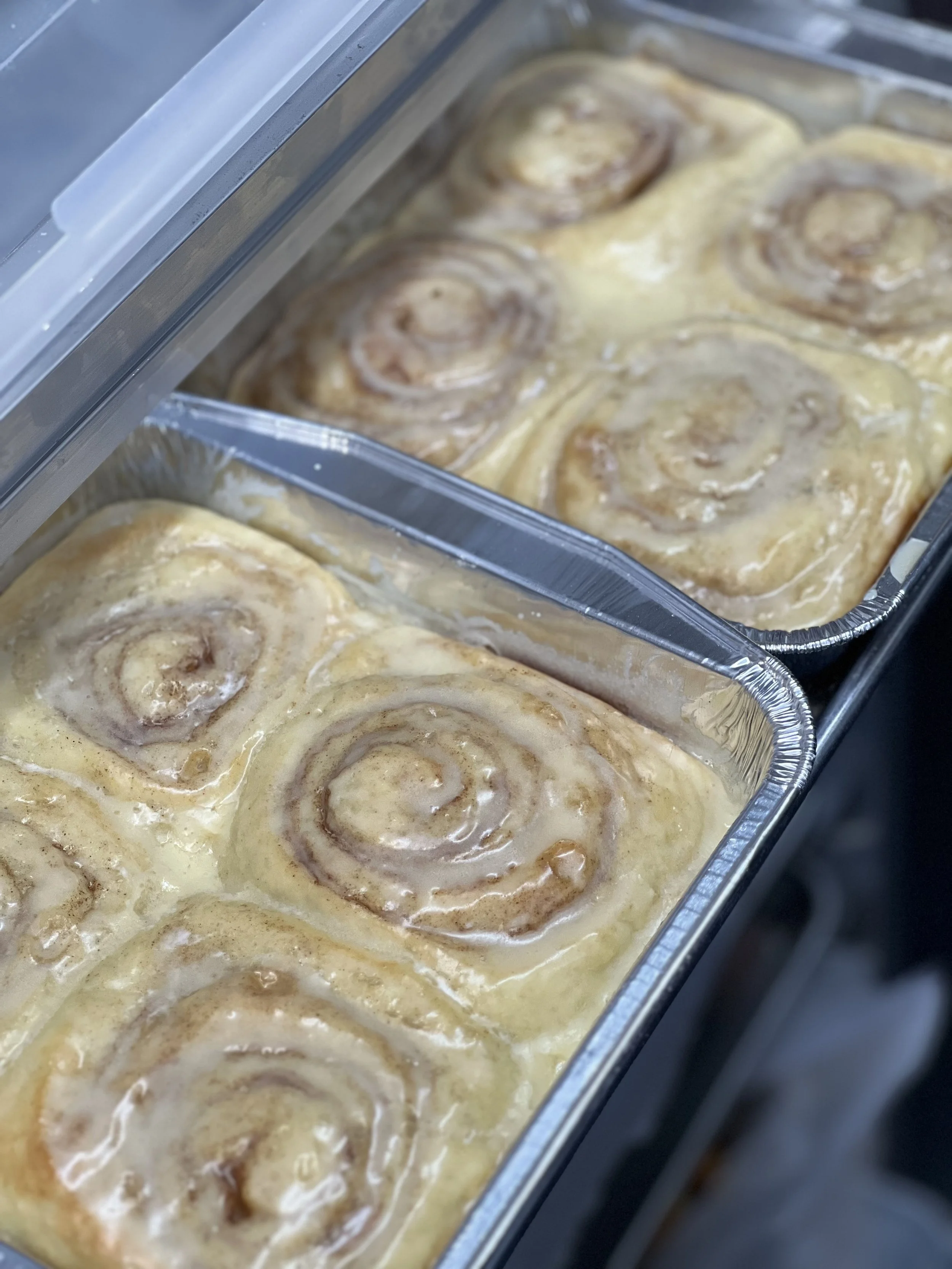 Fresh vanilla-iced cinnamon rolls in bakery trays at Salty Blonde Bakery