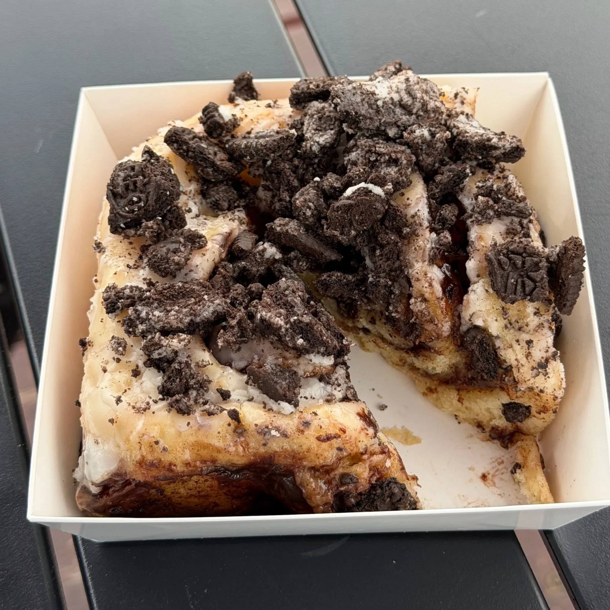 A slice of cookies and cream ice cream cake topped with crushed Oreo cookies in a white box.