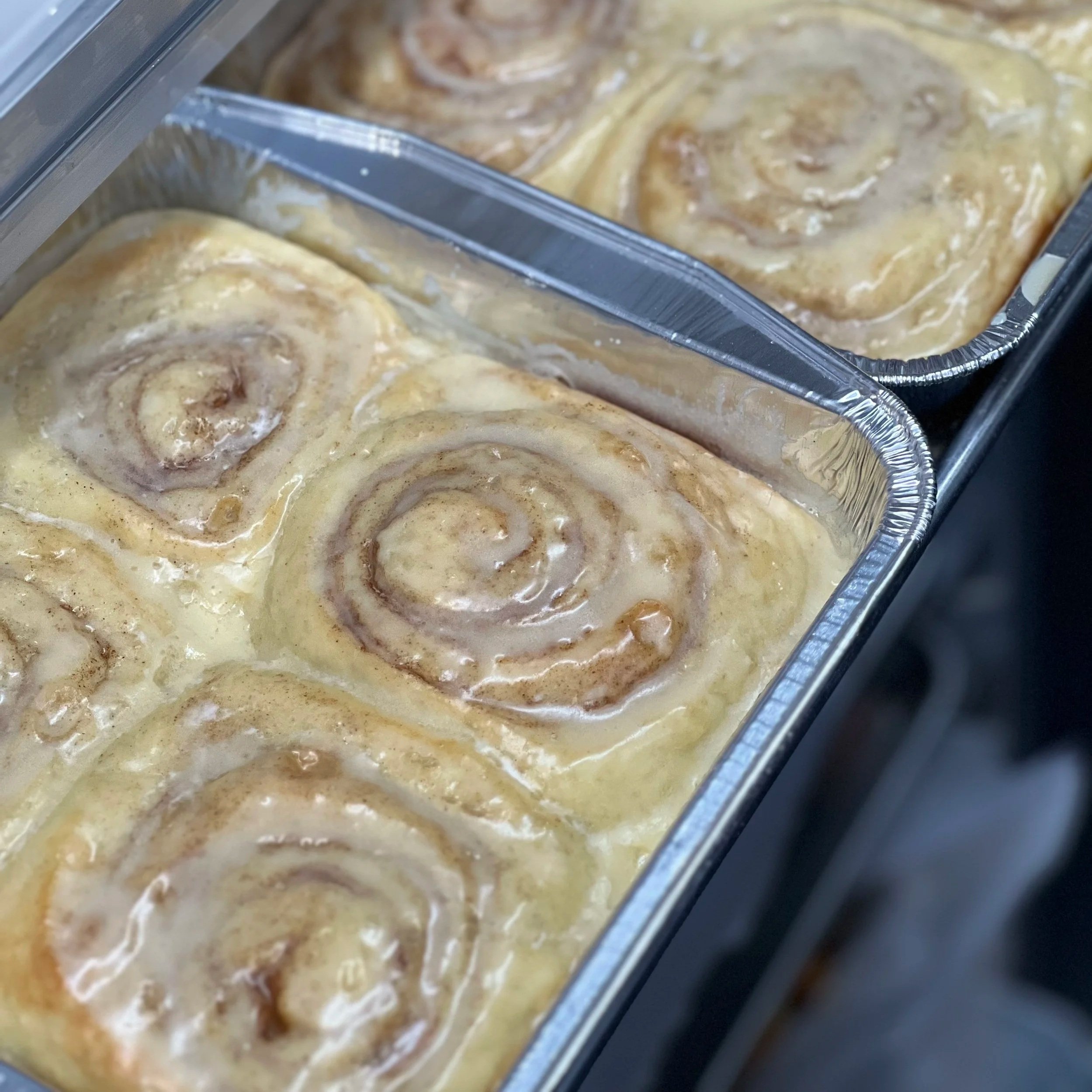 A metal container with several uncooked cinnamon rolls covered in icing.