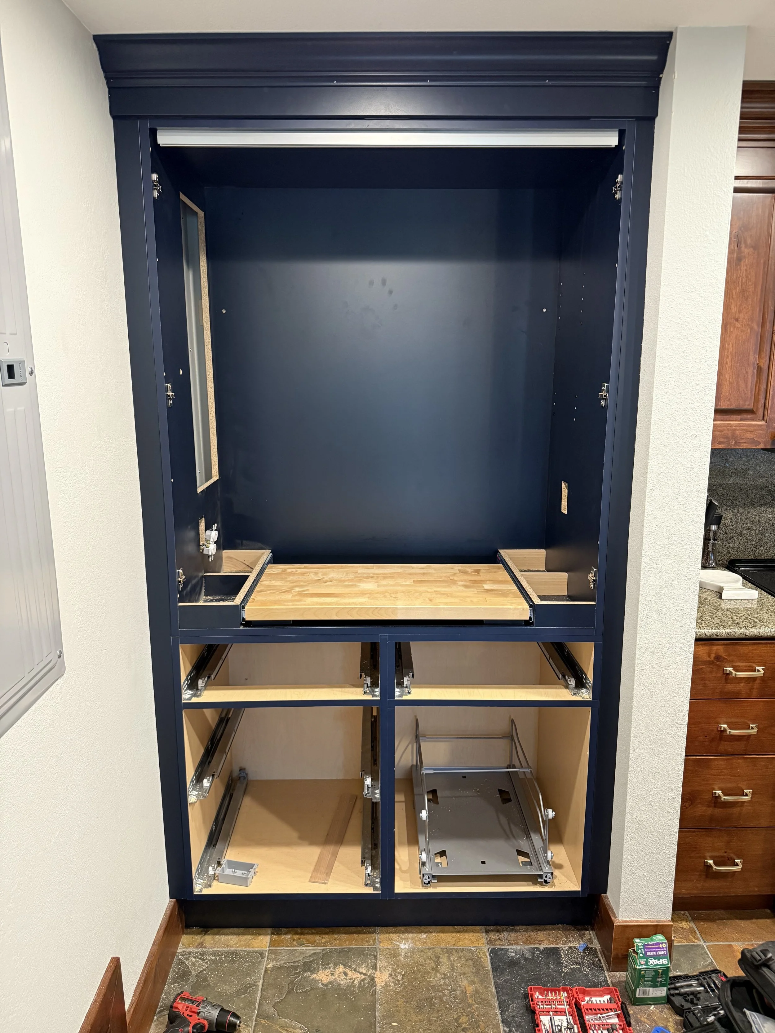 Custom-built navy blue pantry installed in a Park City home, featuring a pull-out butcher block cutting board, integrated electrical outlets, and heavy-duty drawer slides designed for a specific architectural nook