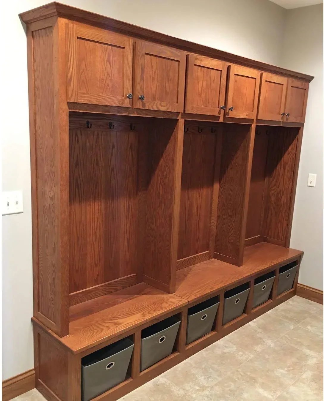 Custom red oak mudroom with integrated ski lockers, oak bench seating, and black metal hooks. Handcrafted furniture-grade entry storage by Utah Craftsman in Park City, Utah.