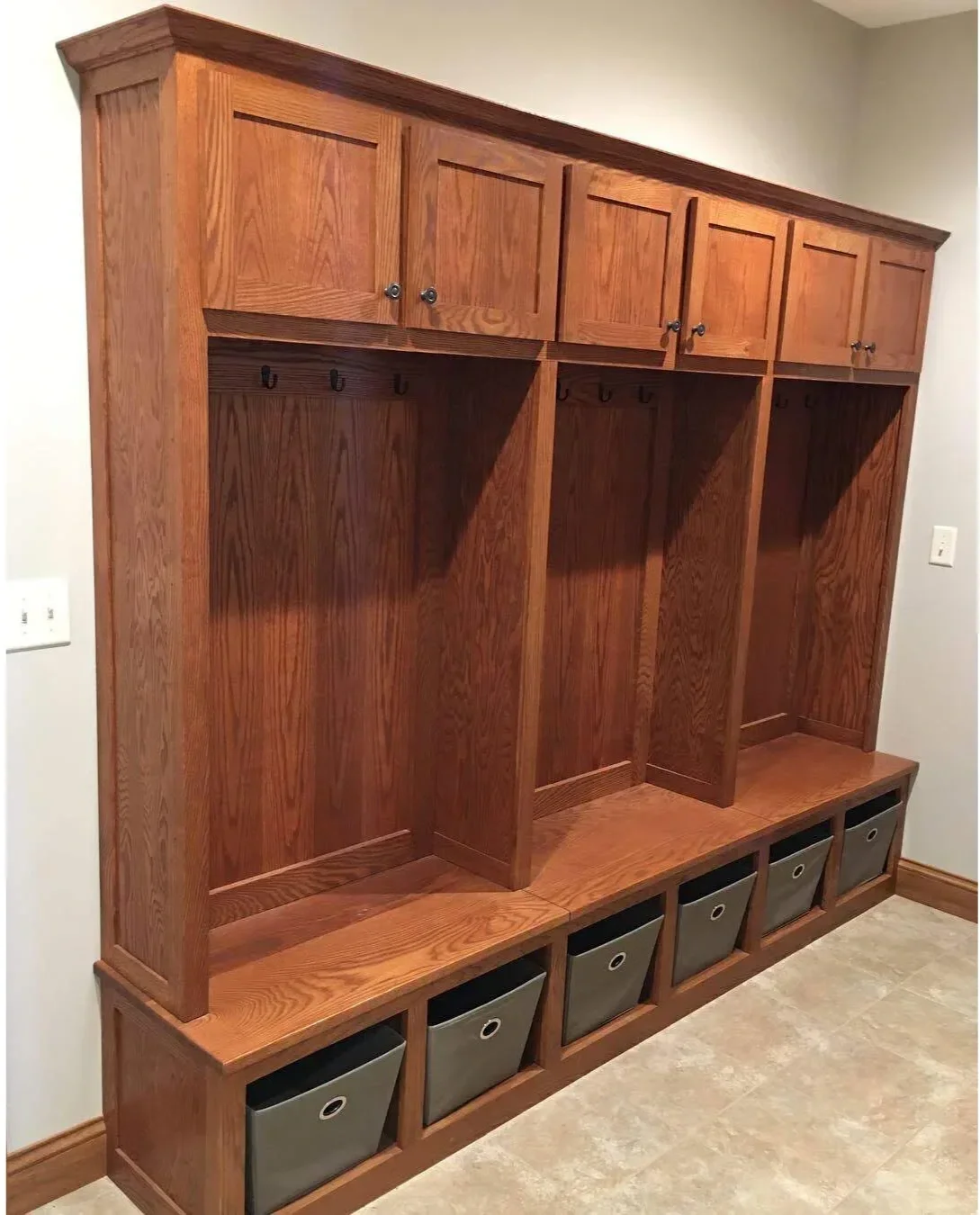 Custom red oak mudroom with integrated ski lockers, oak bench seating, and black metal hooks. Handcrafted furniture-grade entry storage by Utah Craftsman in Park City, Utah.