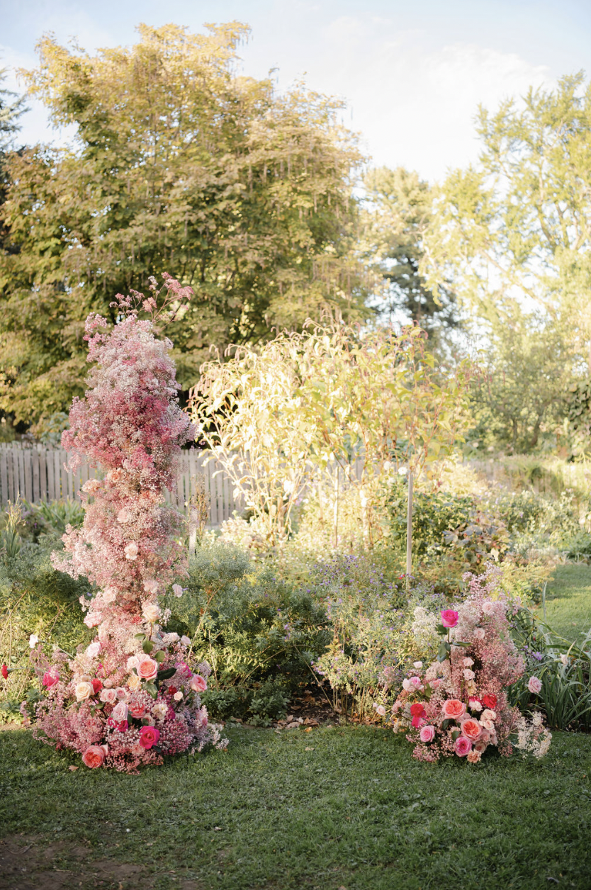 Colorful floral arrangement in a garden with pink and red flowers and lush greenery under sunlight.