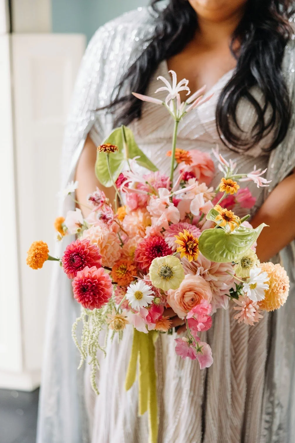 A woman holding a colorful bouquet of various flowers, including dahlias, roses, and daisies, with greenery and a yellow ribbon.