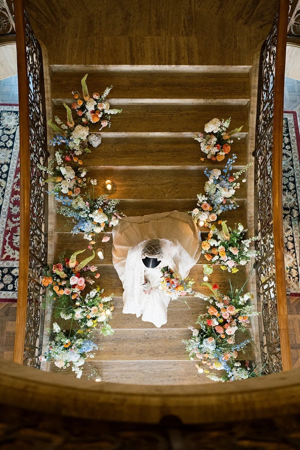 A couple kissing at the top of a wooden staircase decorated with colorful flowers.