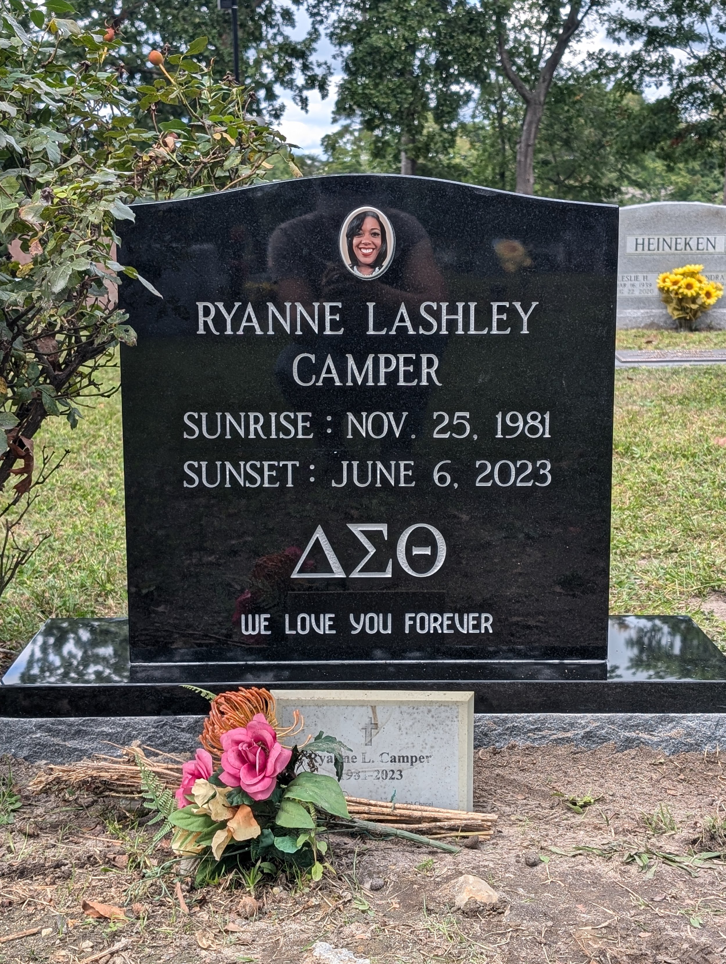 Gravestone of Ryanne Lashely Camper with her photo, birth and death dates, Greek letters Delta Sigma Theta, and the message "We love you forever." Flower bouquet and smaller headstone at the base.