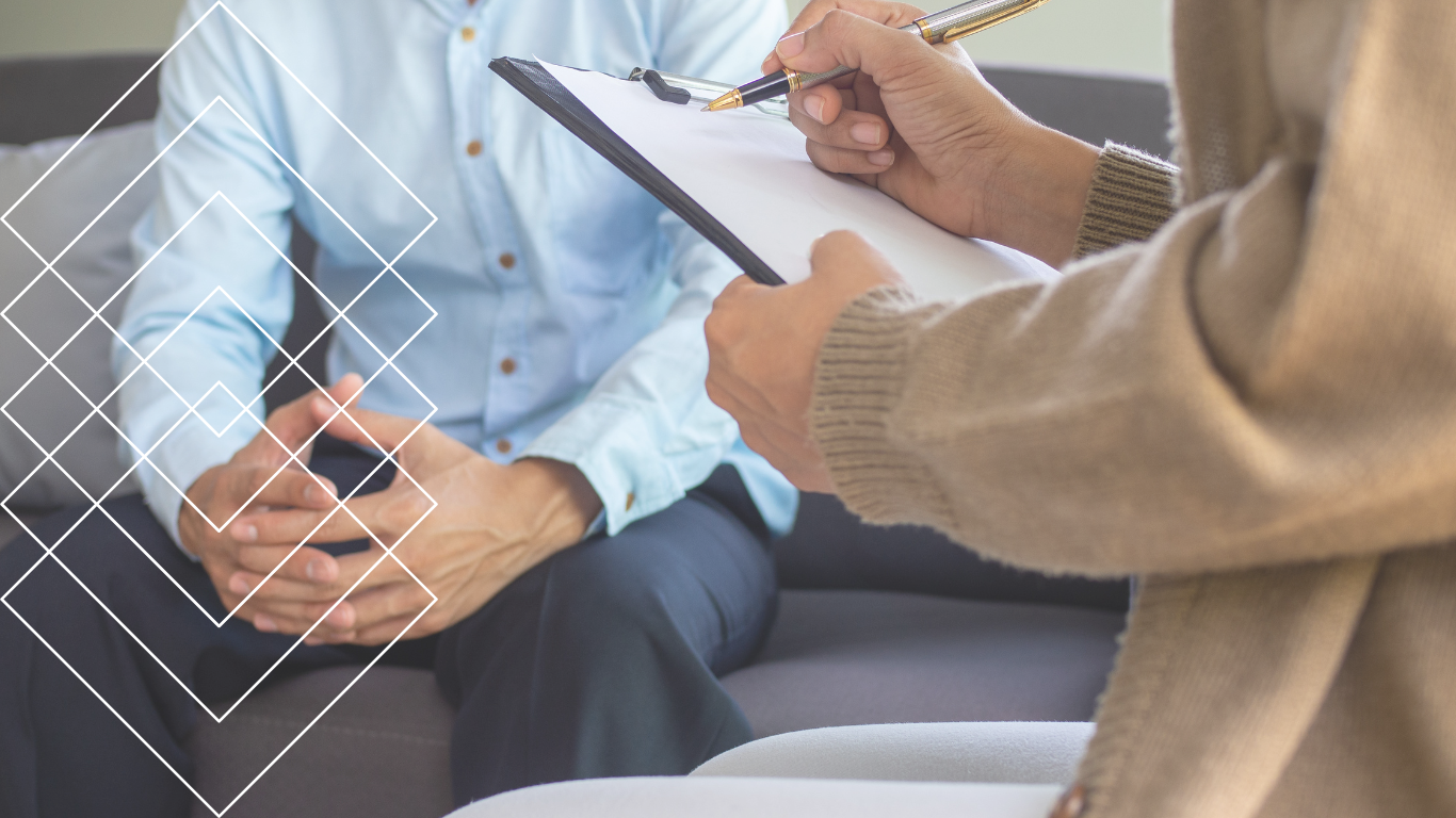 Person taking notes on a clipboard during a consultation with a seated patient, who is holding a smartphone, in a medical or counseling setting.
