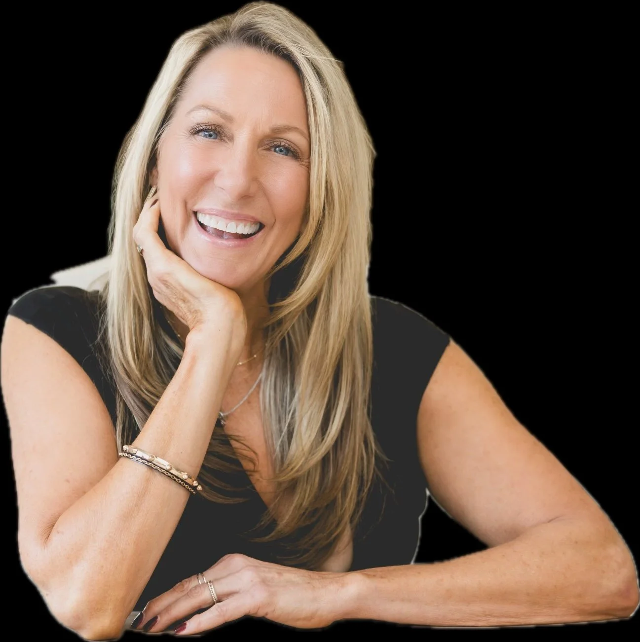 Smiling woman with long blonde hair, wearing a black top, hand resting on chin, against a black background.