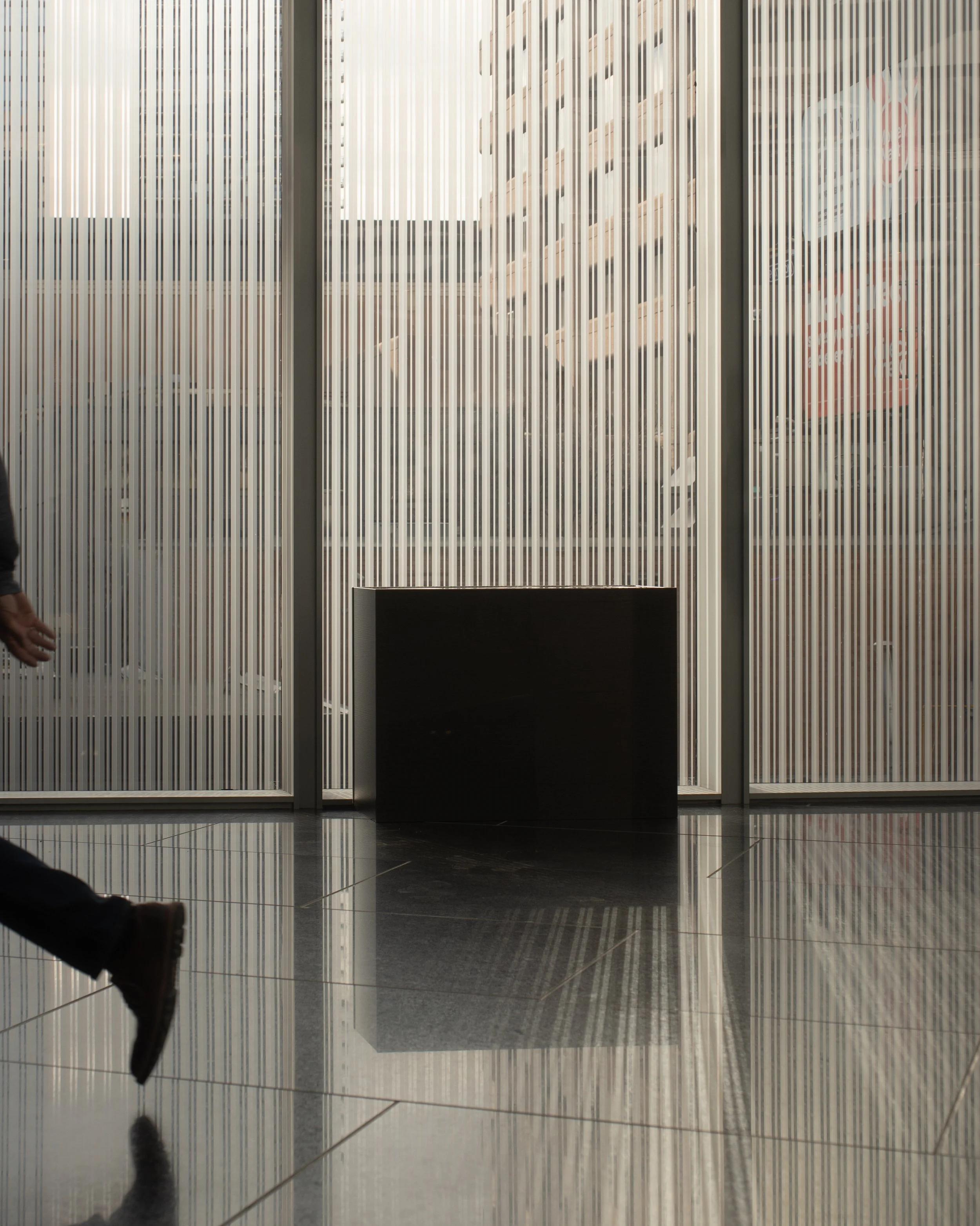 Interior view of a modern building with frosted glass walls and a black rectangular bench on a reflective tile floor.