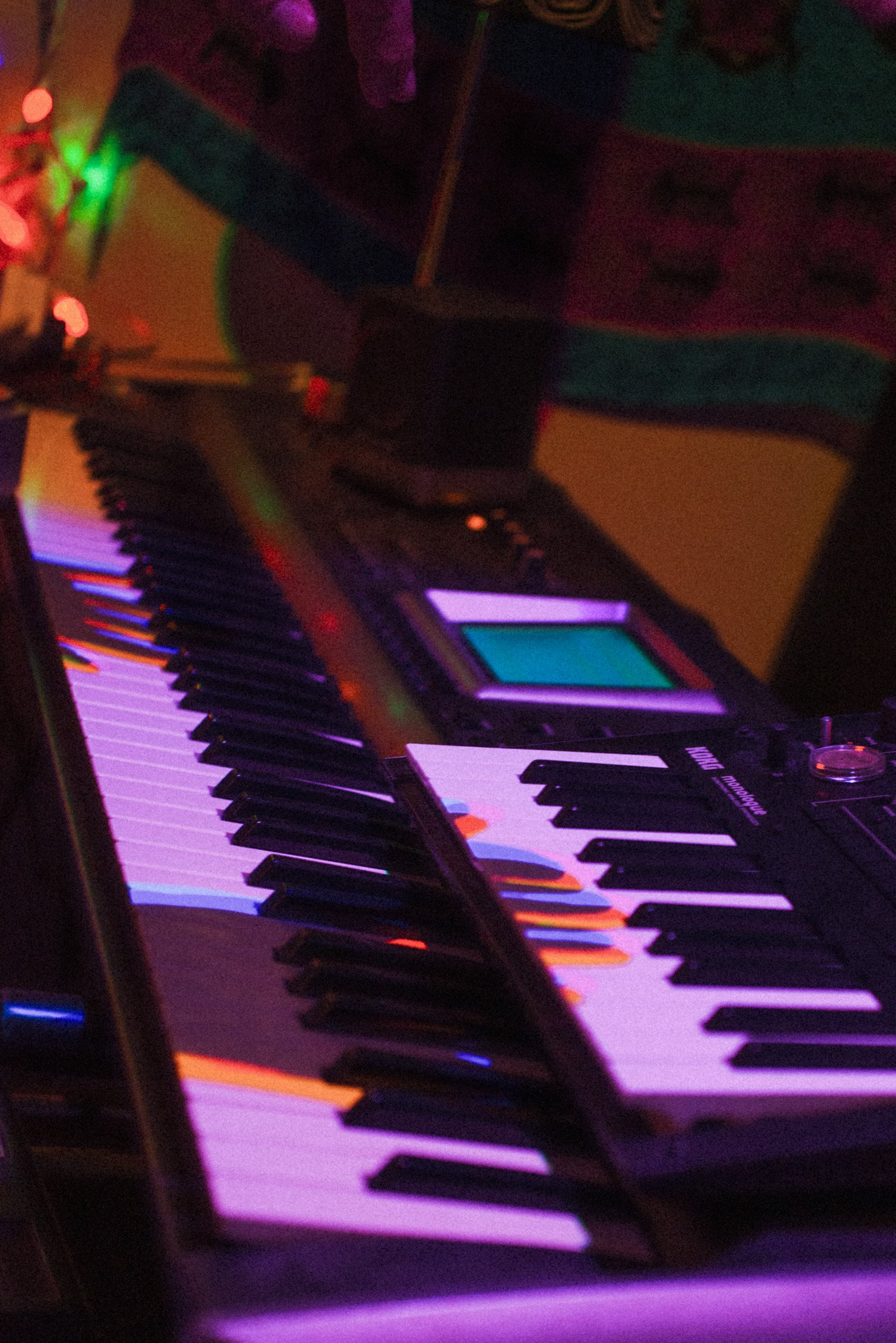 Close-up of a colorful keyboard and electronic music equipment illuminated by vibrant lights.