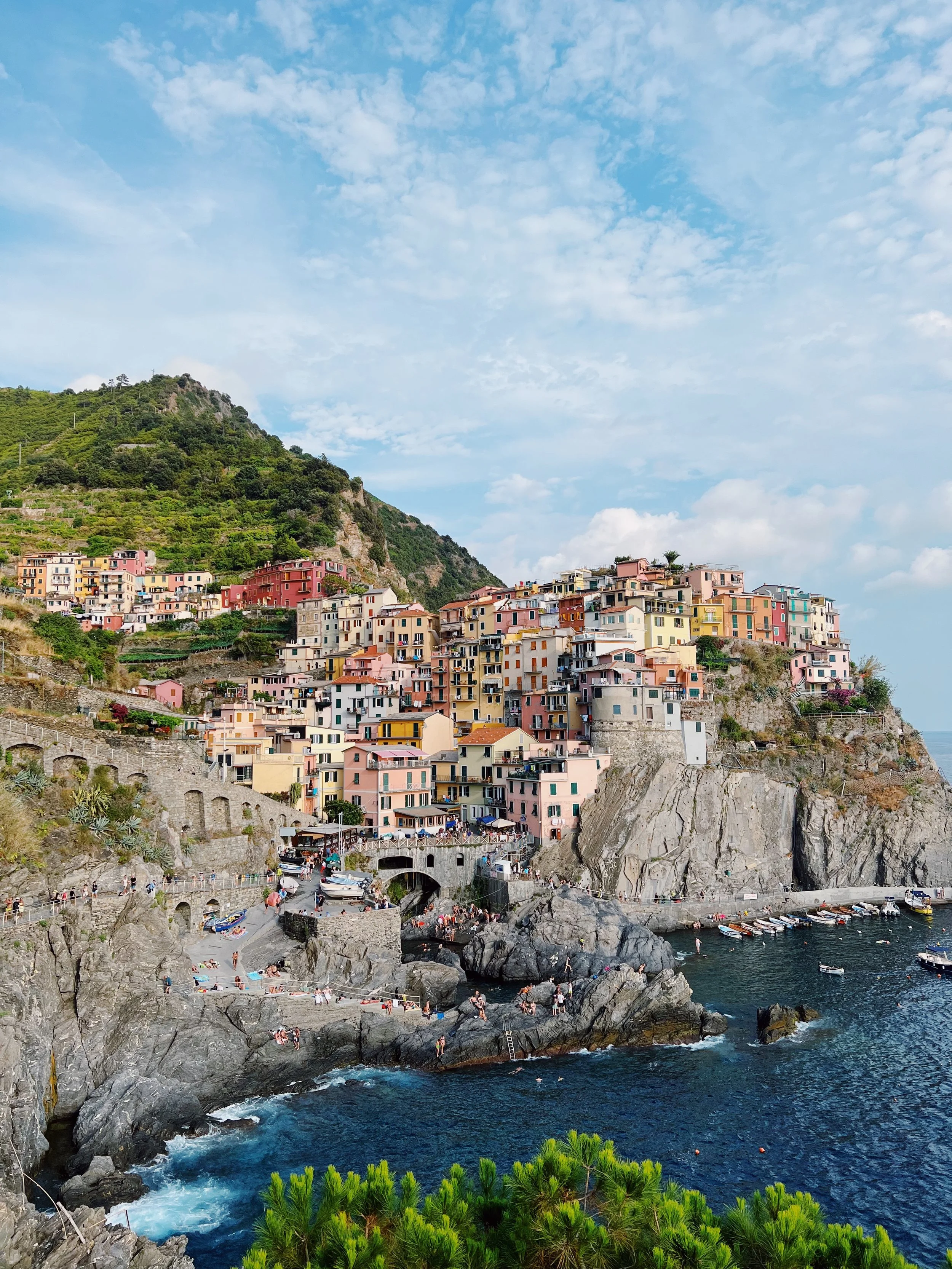 Colorful buildings on a hillside overlooking the blue sea with boats, under a partly cloudy sky.