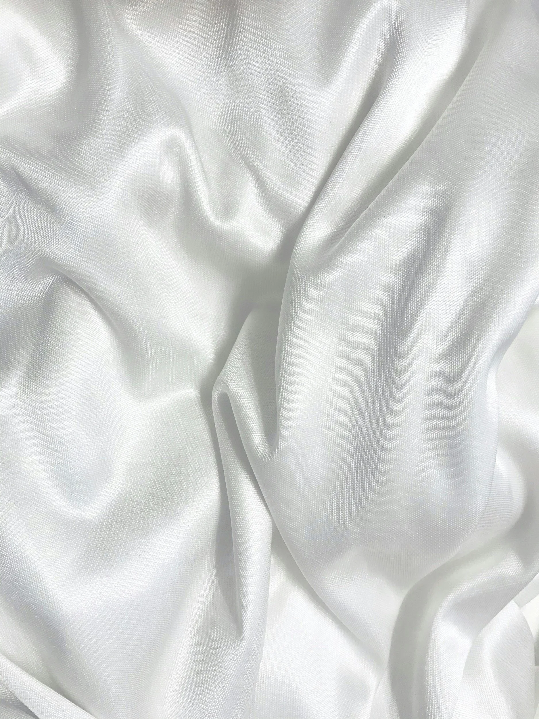 Close-up of smooth, white silk fabric with folds and soft texture.