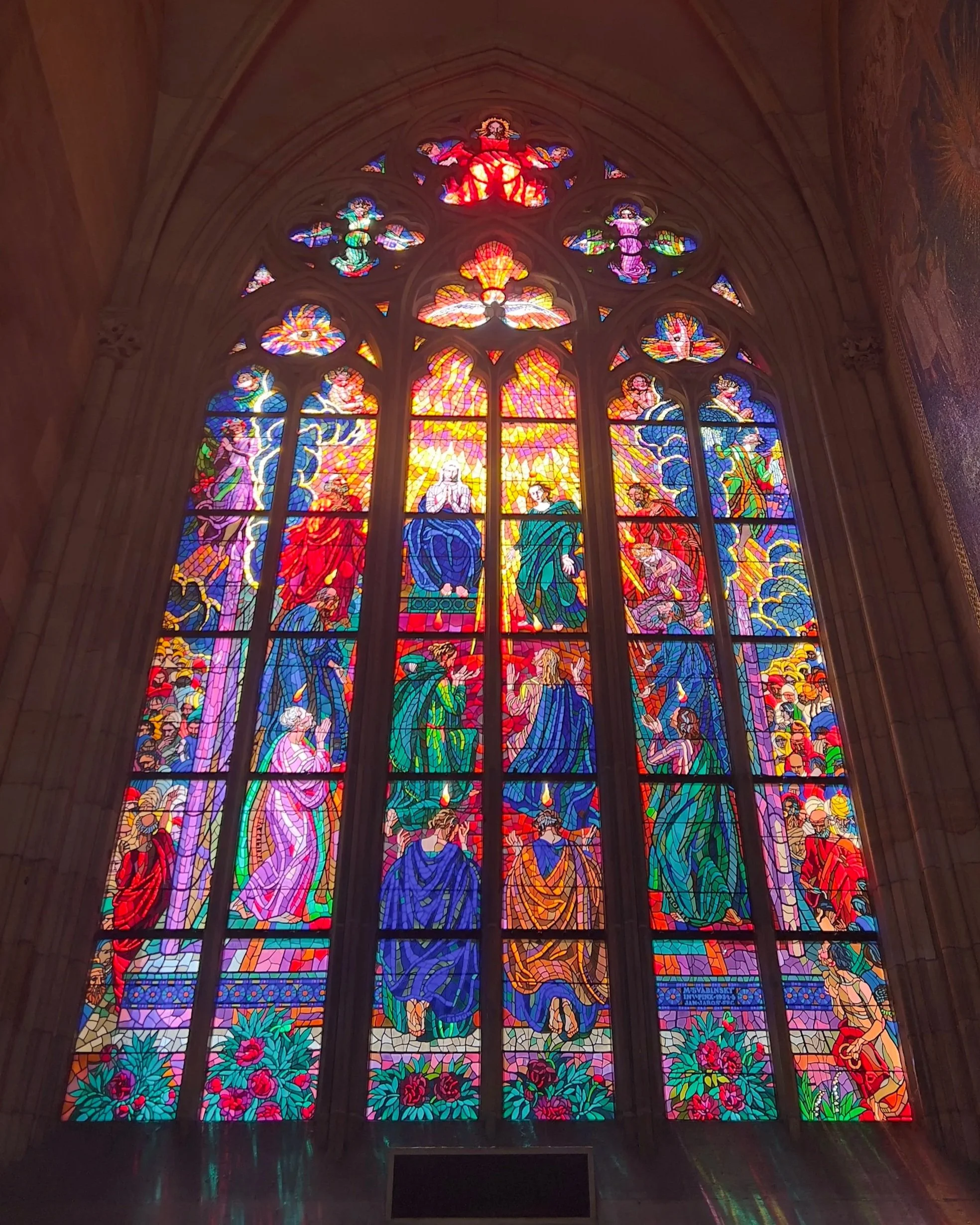 Colorful stained glass window depicting religious figures and scenes, with intricate designs and vibrant colors.