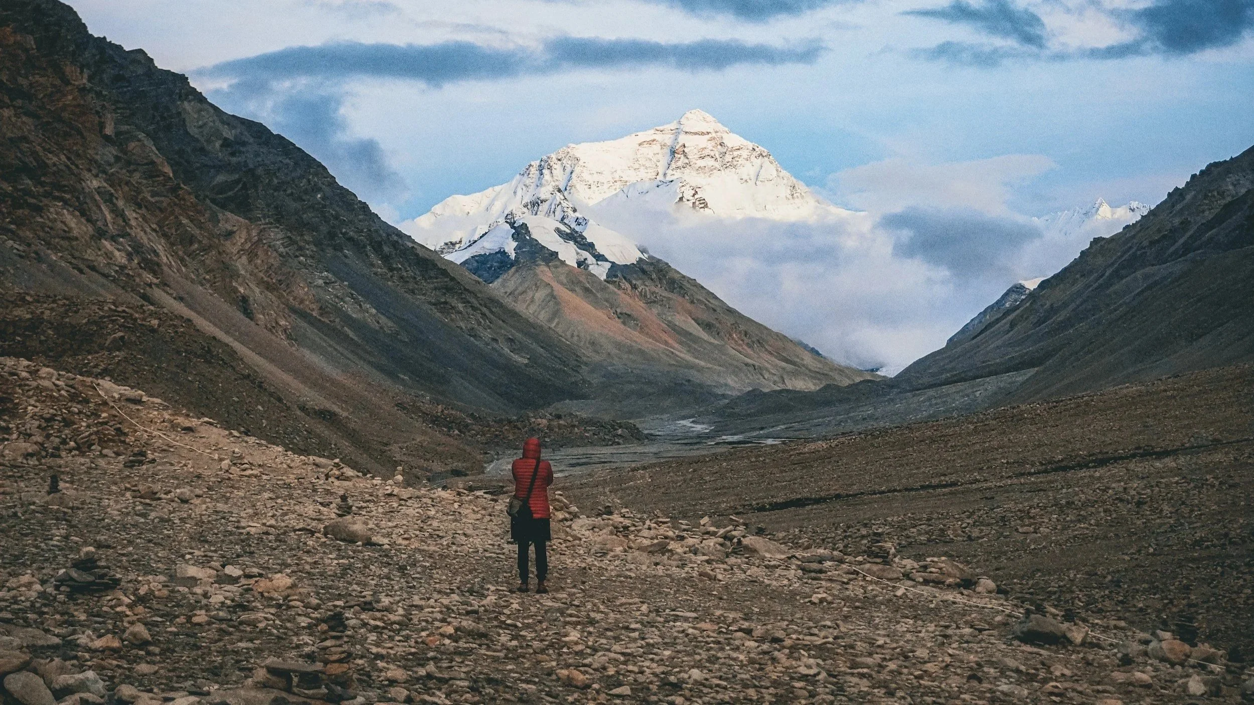 person wearing red jacket while hiking hiking mount everest looking at the peak ahead