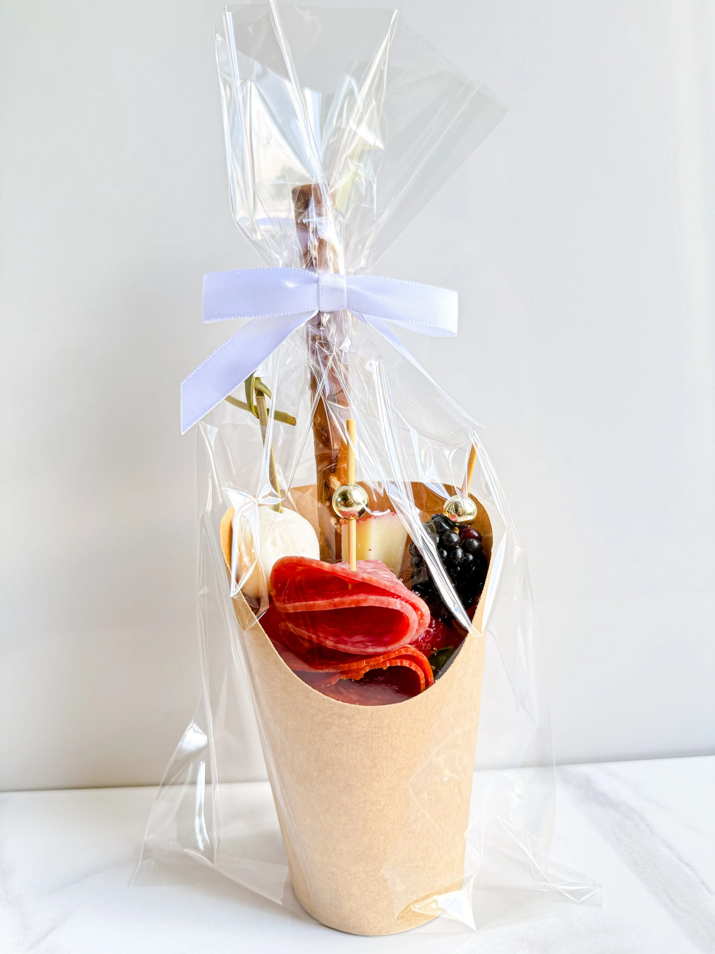 Individual charcuterie cup with meats, cheeses, fresh fruit, and a pretzel rod.