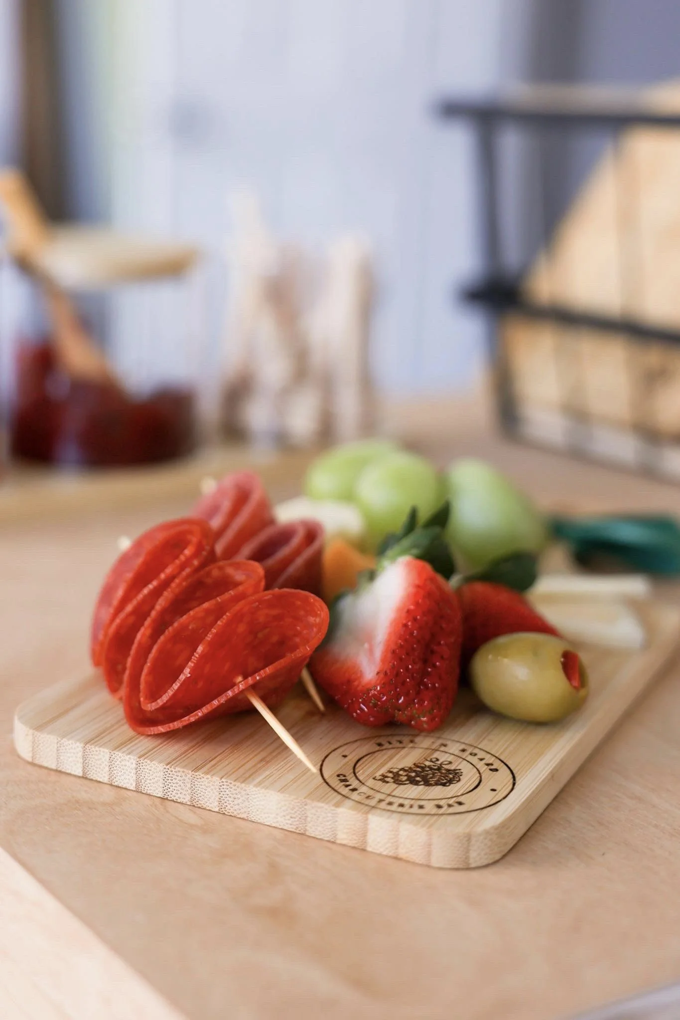Meat and fruit displayed on a bamboo charcuterie board branded with logo