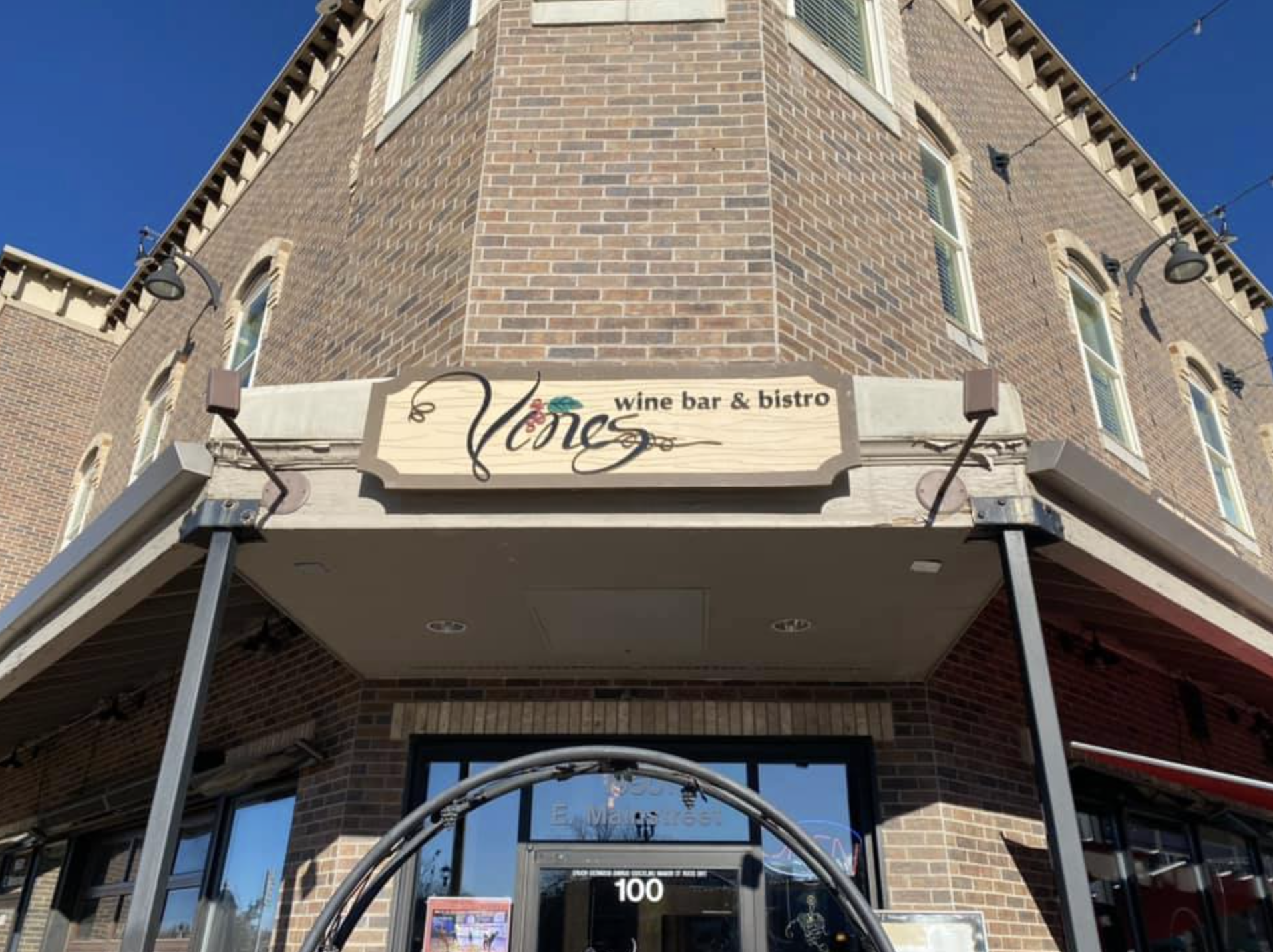 Sign on brick building reading 'Vines wine bar & bistro' with an entrance below and windows above on a clear day.