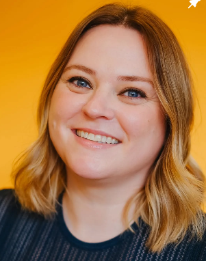 Portrait of a smiling woman with shoulder-length blonde hair and blue eyes, against a yellow background.
